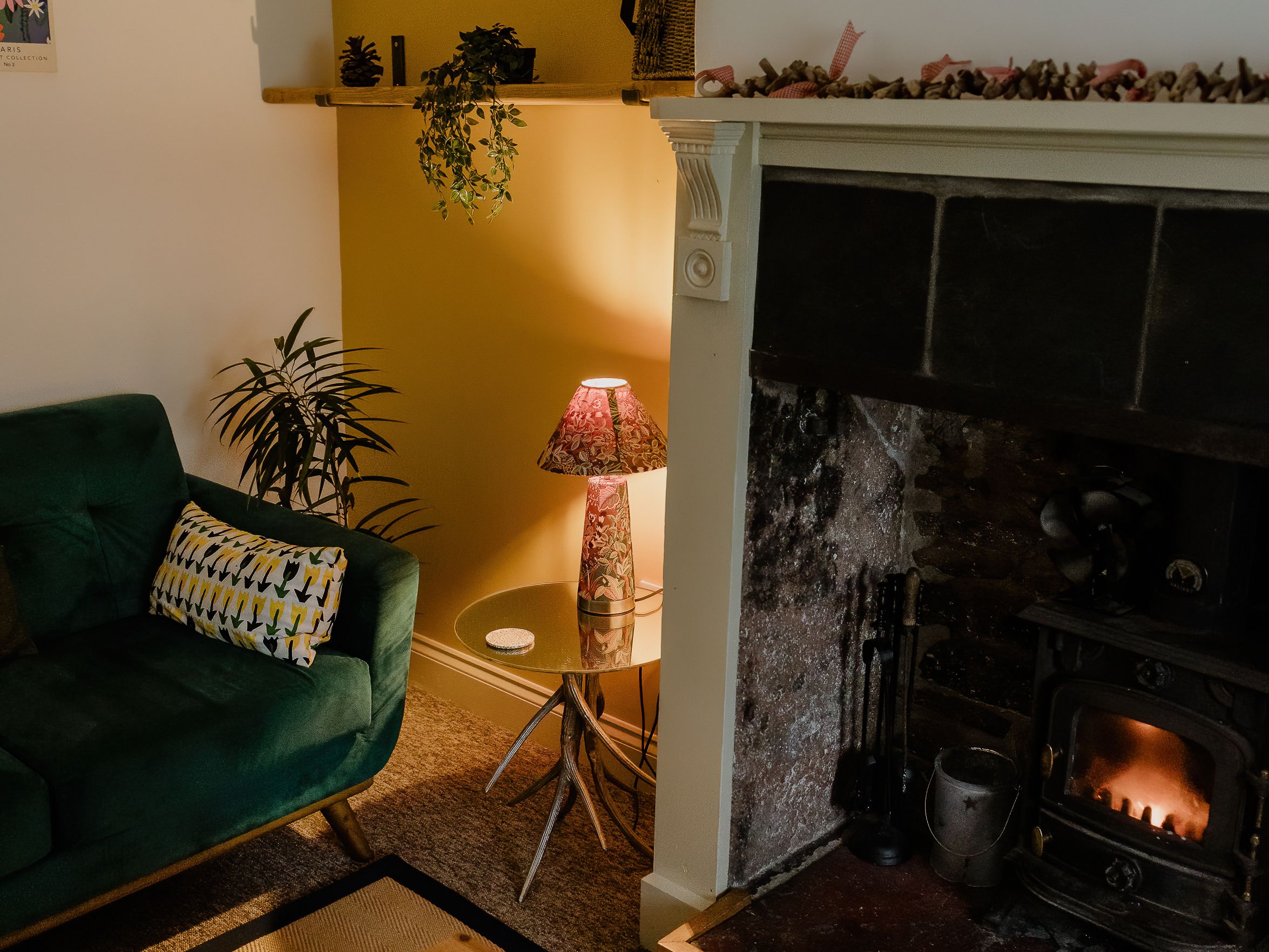 Cosy living room corner with green armchair, lit stove fireplace and warm lamp