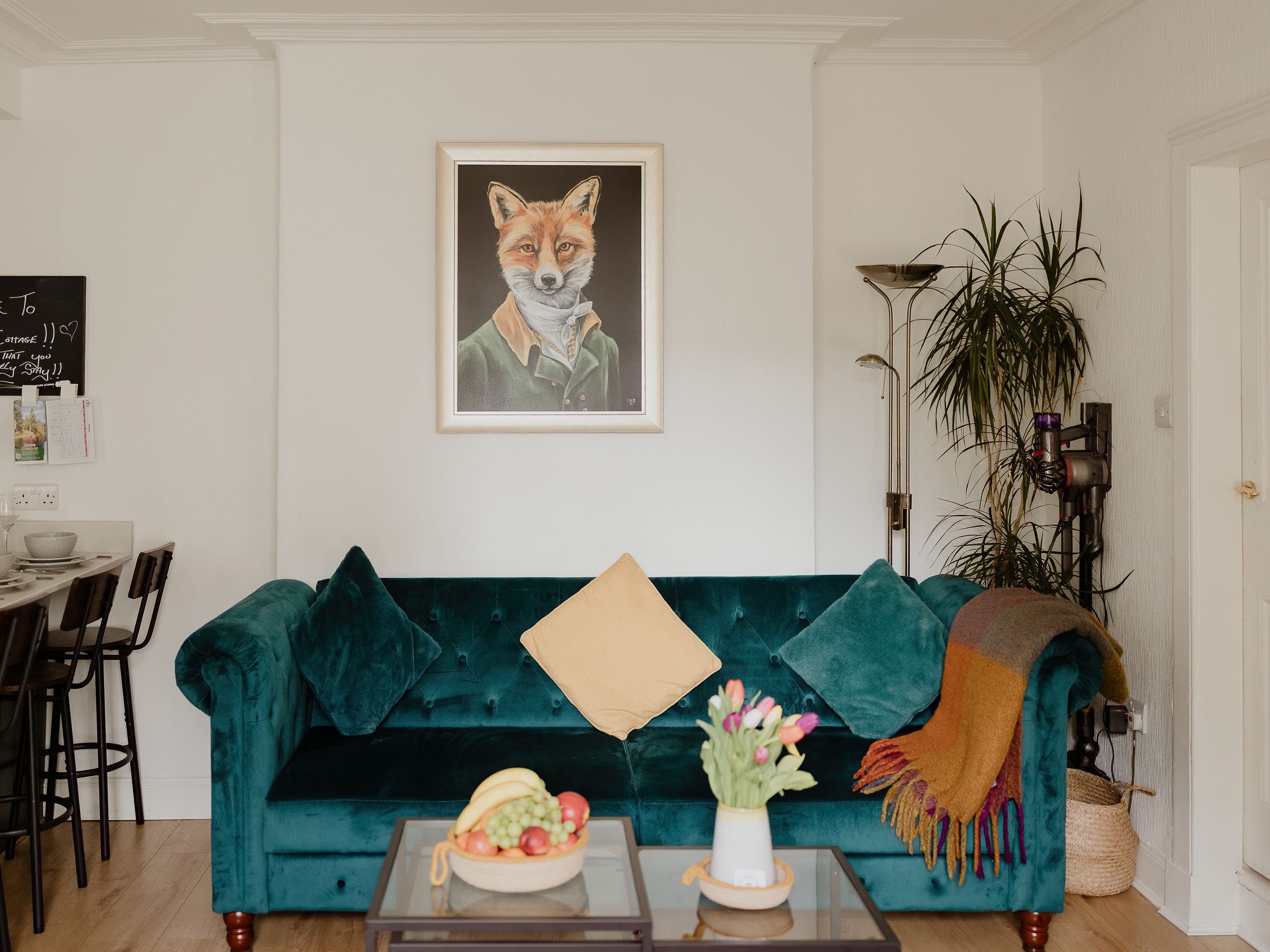 Cosy living room with teal velvet sofa, dining table set for six, and framed fox portrait on the wall