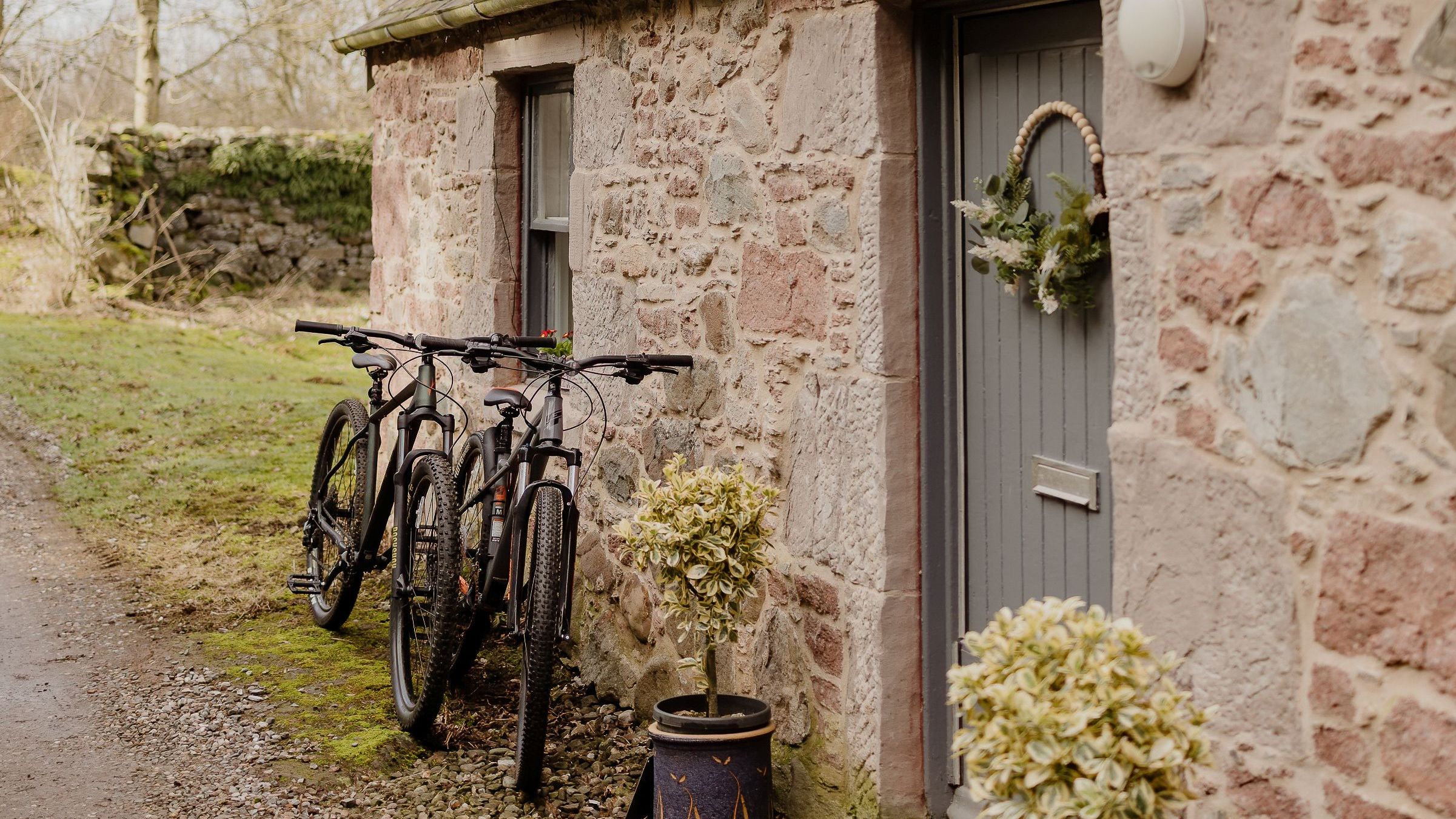 Stone cottage exterior with two bicycles by a grey door and wreath