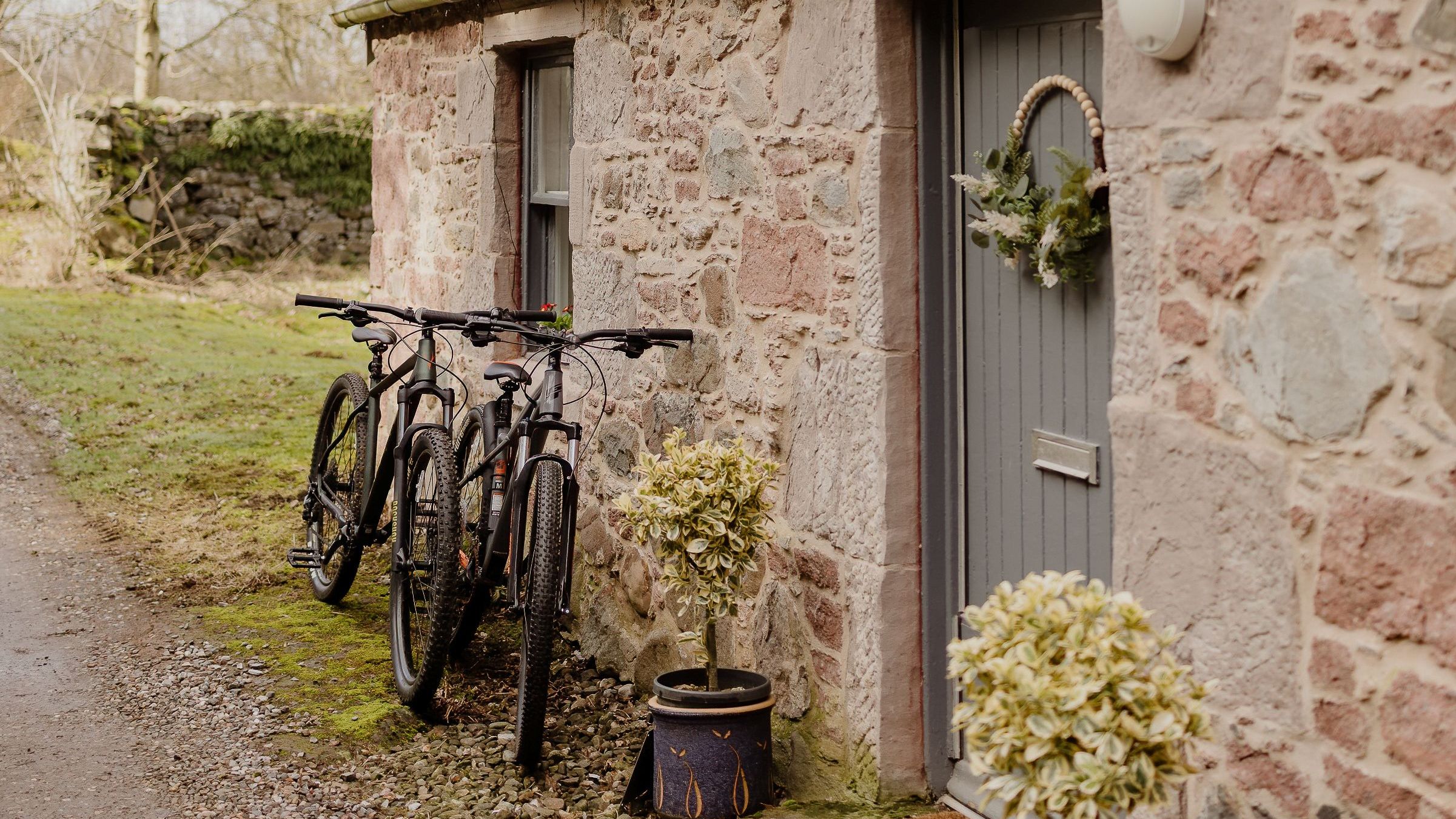 Stone cottage exterior with two bicycles by a grey door and wreath