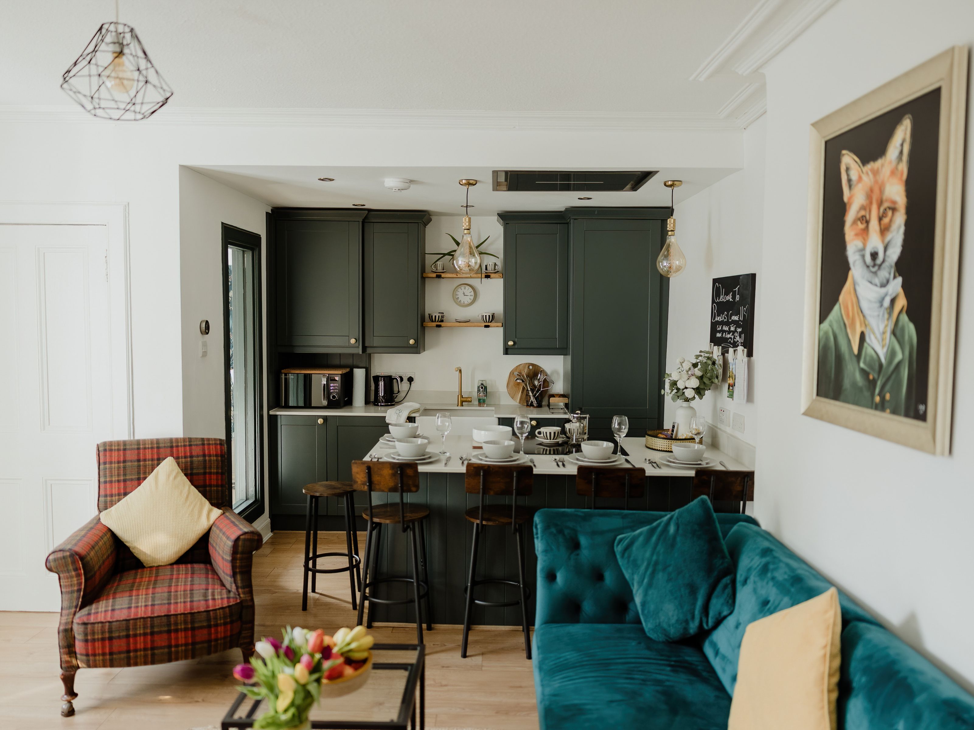 Cosy open-plan living room and kitchen with dark green cabinets, breakfast bar, teal sofa and fox wall art