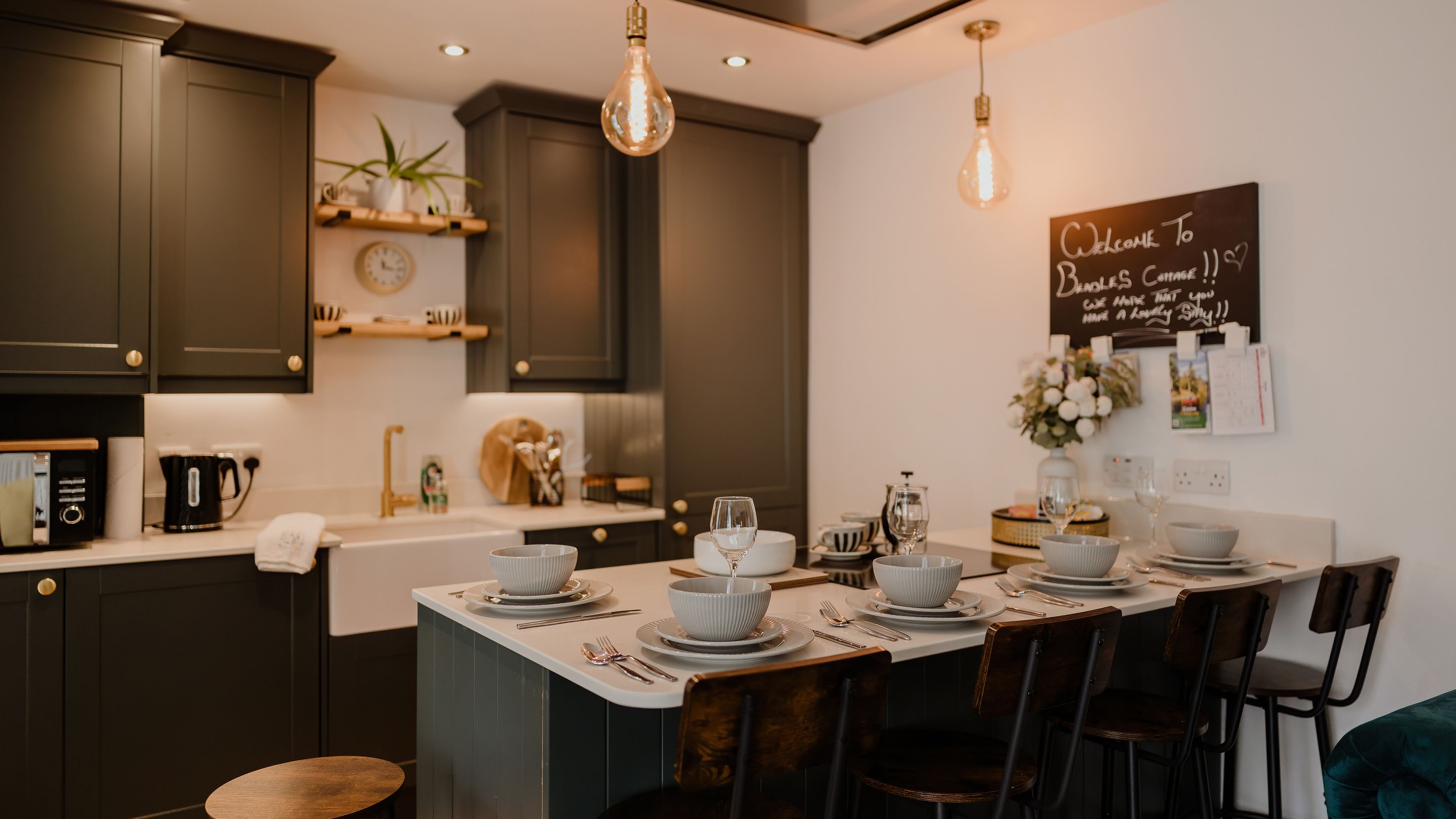 Modern kitchen with dark grey cabinets, pendant lights and a dining island set with tableware