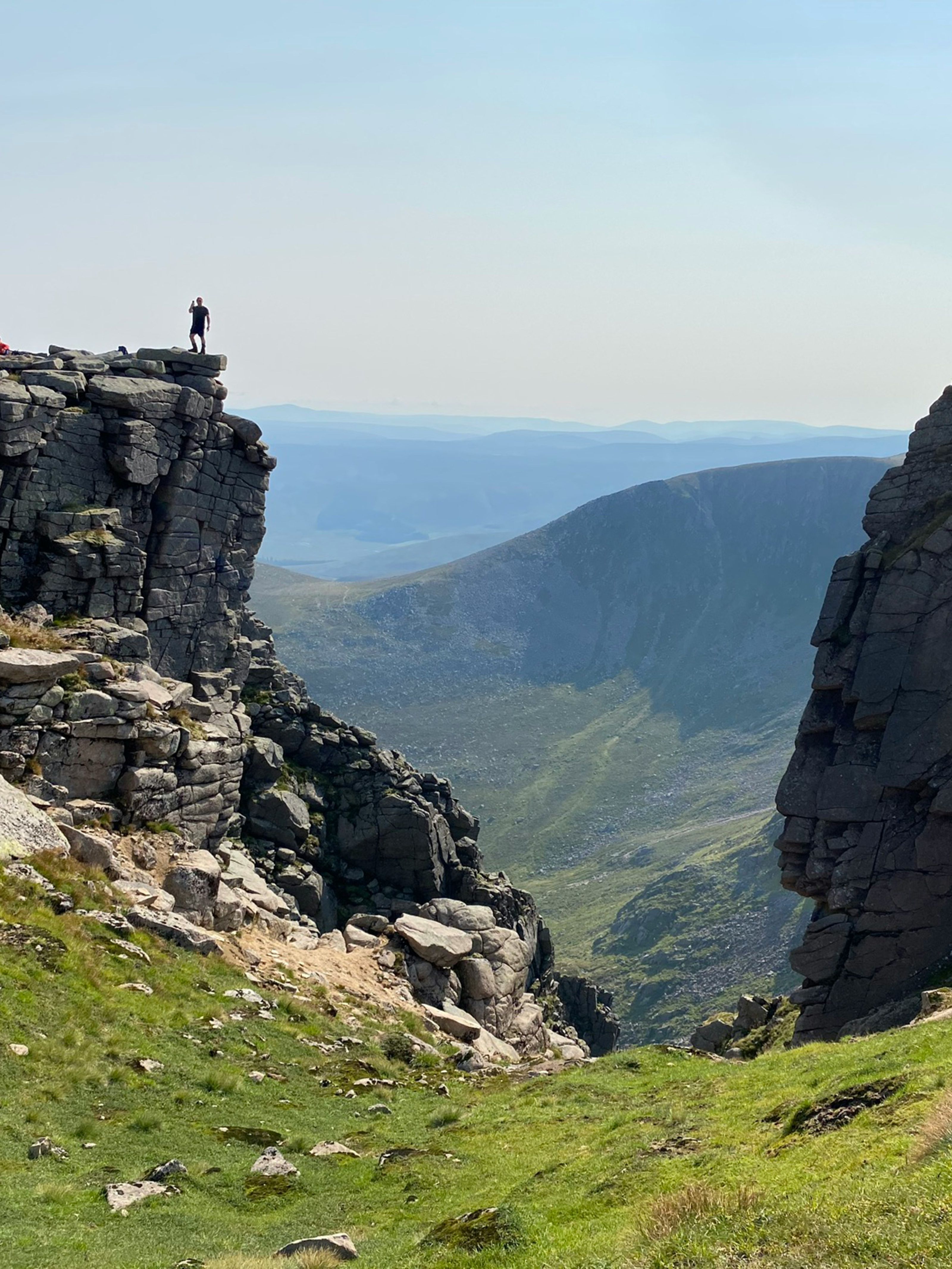 Hiker standing on a rocky cliff overlooking a deep mountain valley under a clear sky