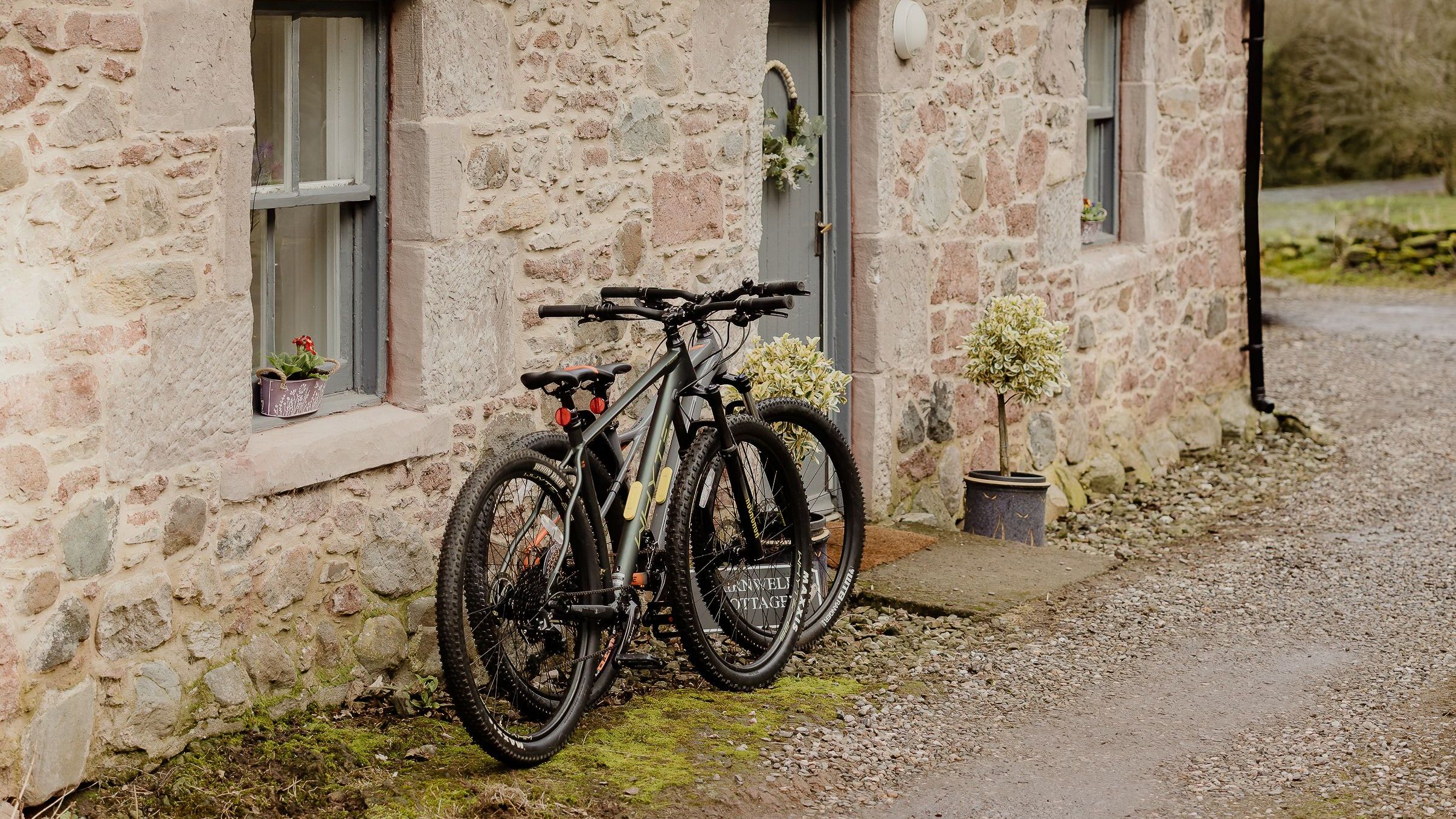 Two bicycles leaning against a stone cottage with a slate roof
