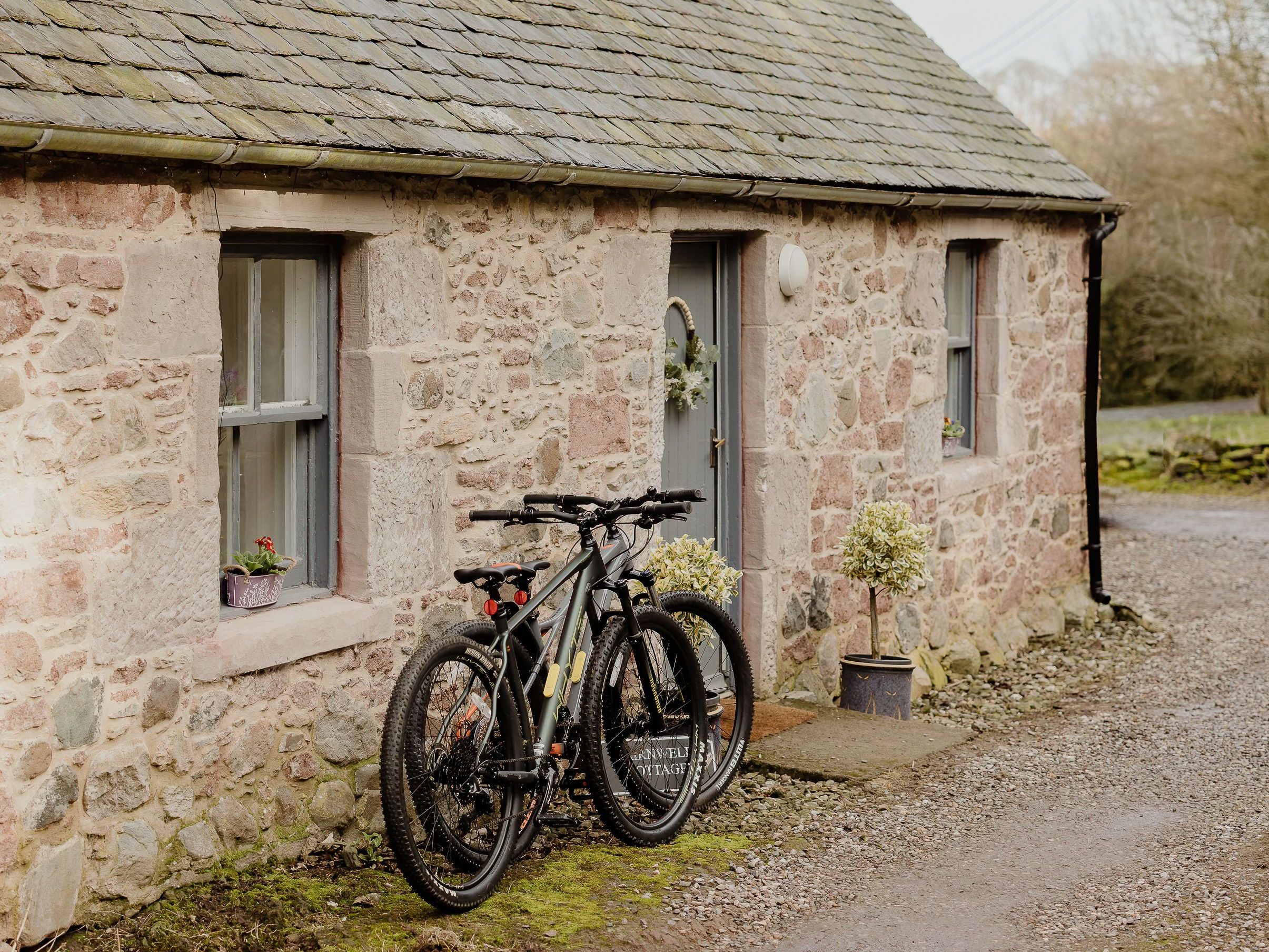 Two bicycles leaning against a stone cottage with a slate roof