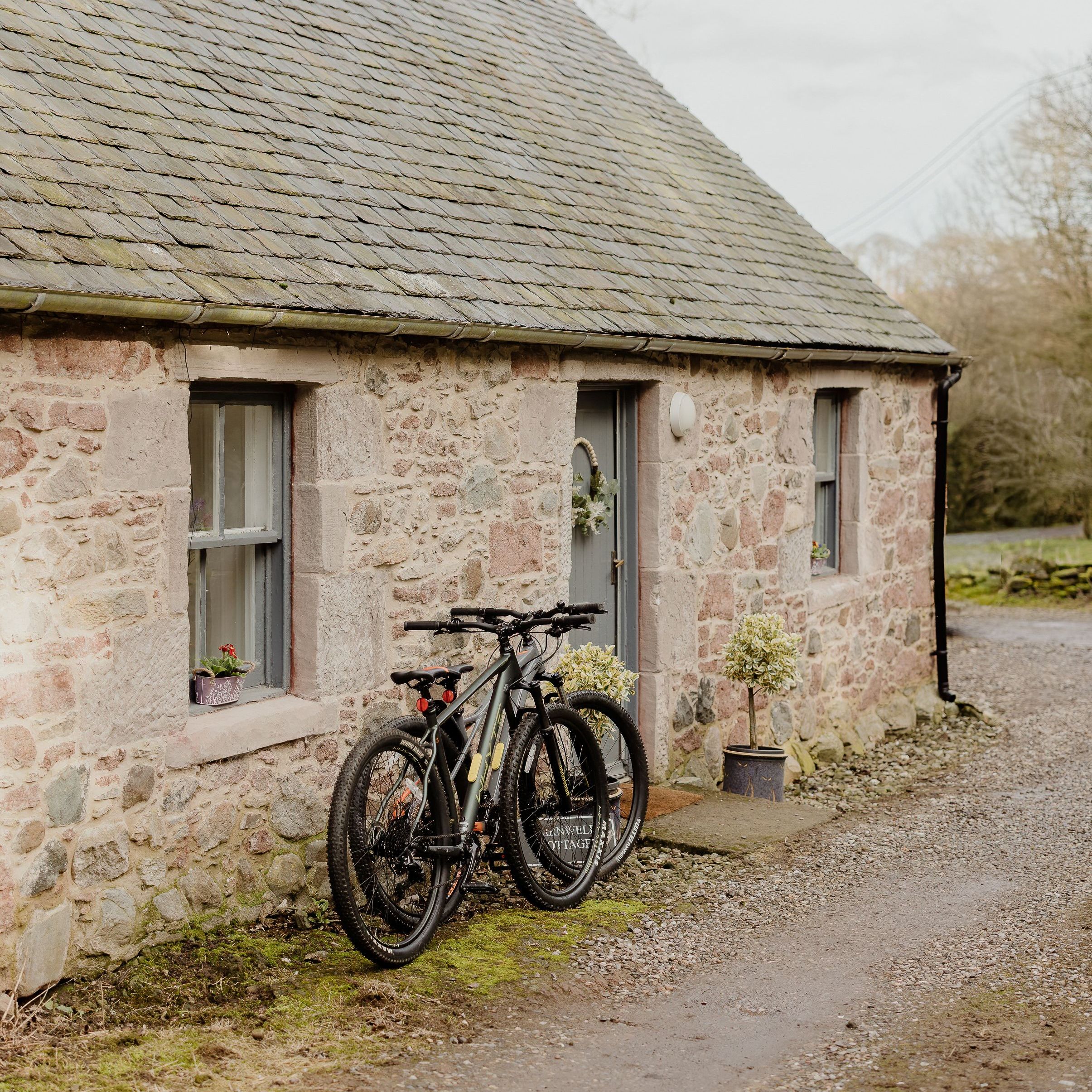 Two bicycles leaning against a stone cottage with a slate roof