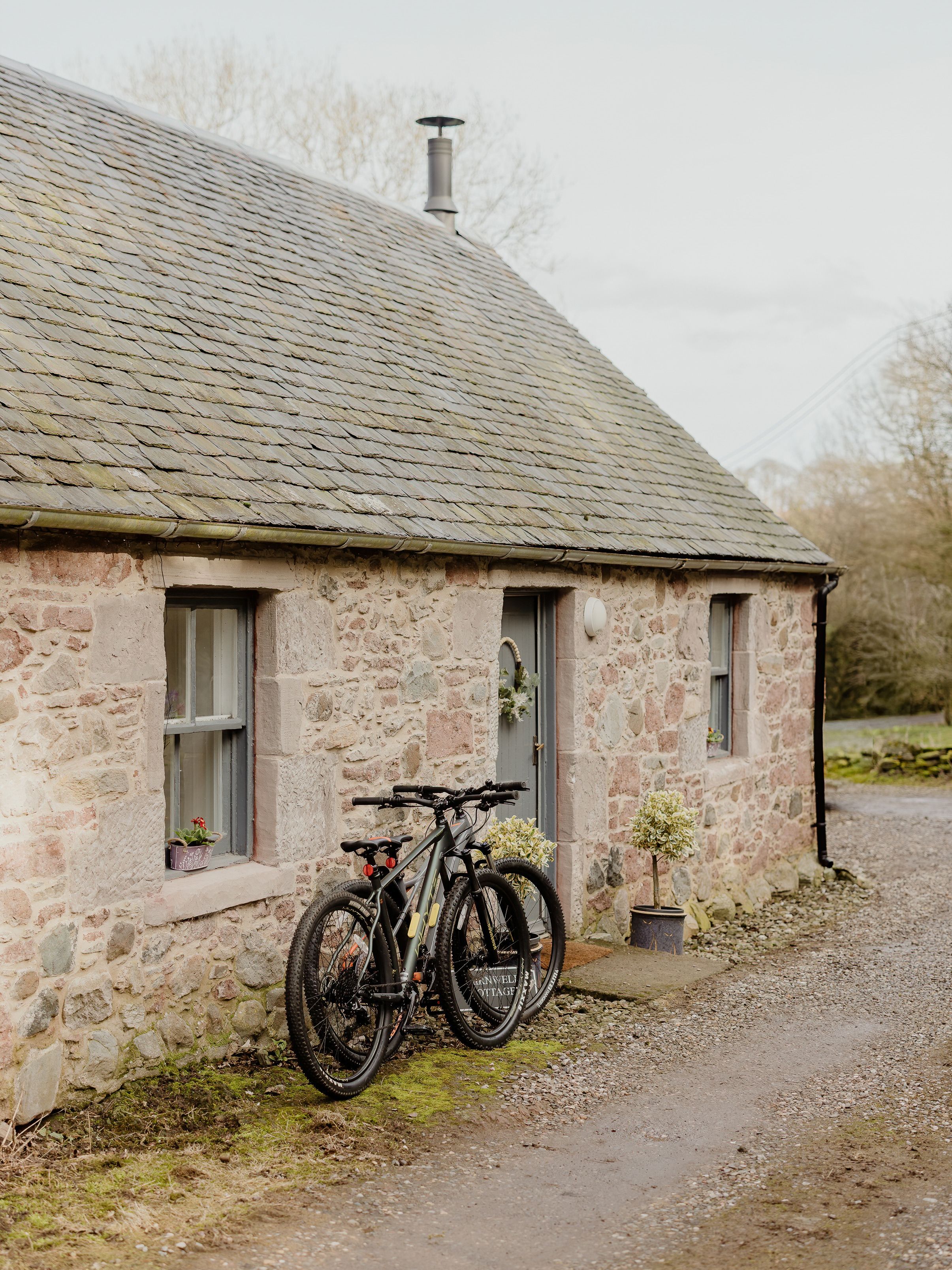 Two bicycles leaning against a stone cottage with a slate roof