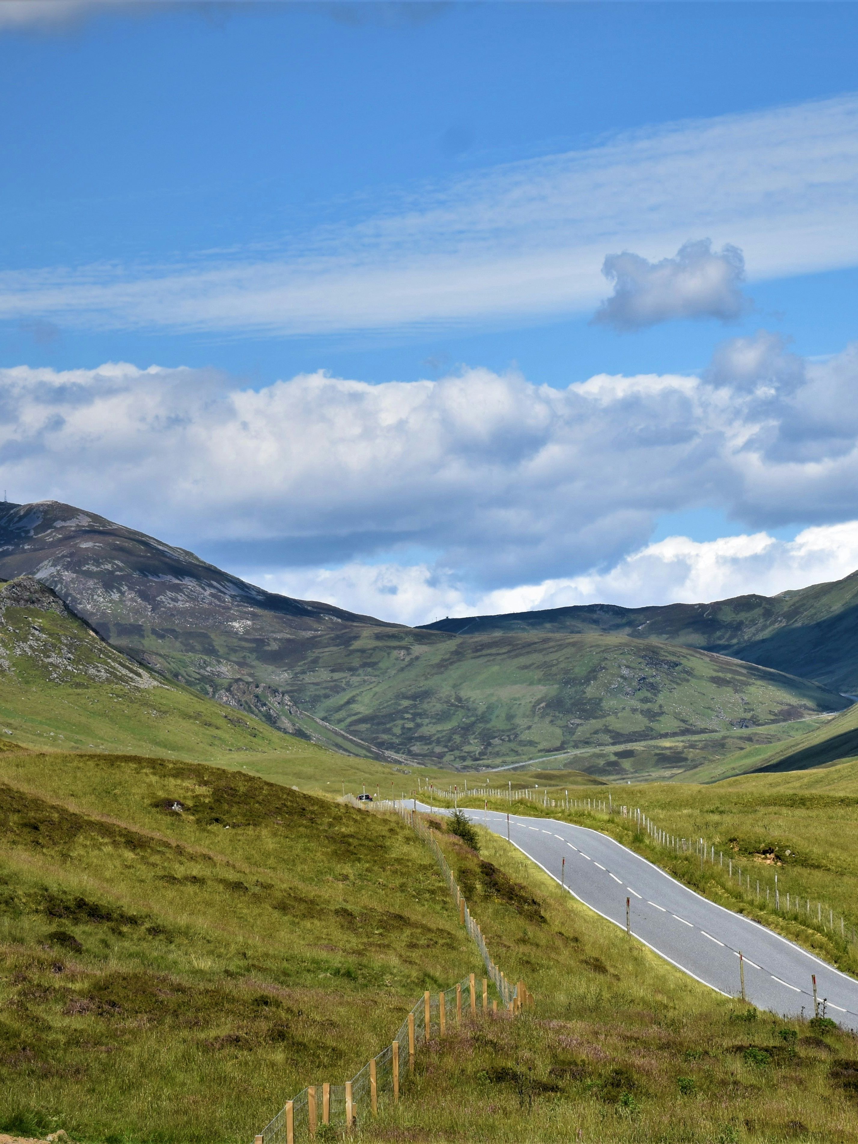 Winding road through rolling green hills under a blue sky with clouds