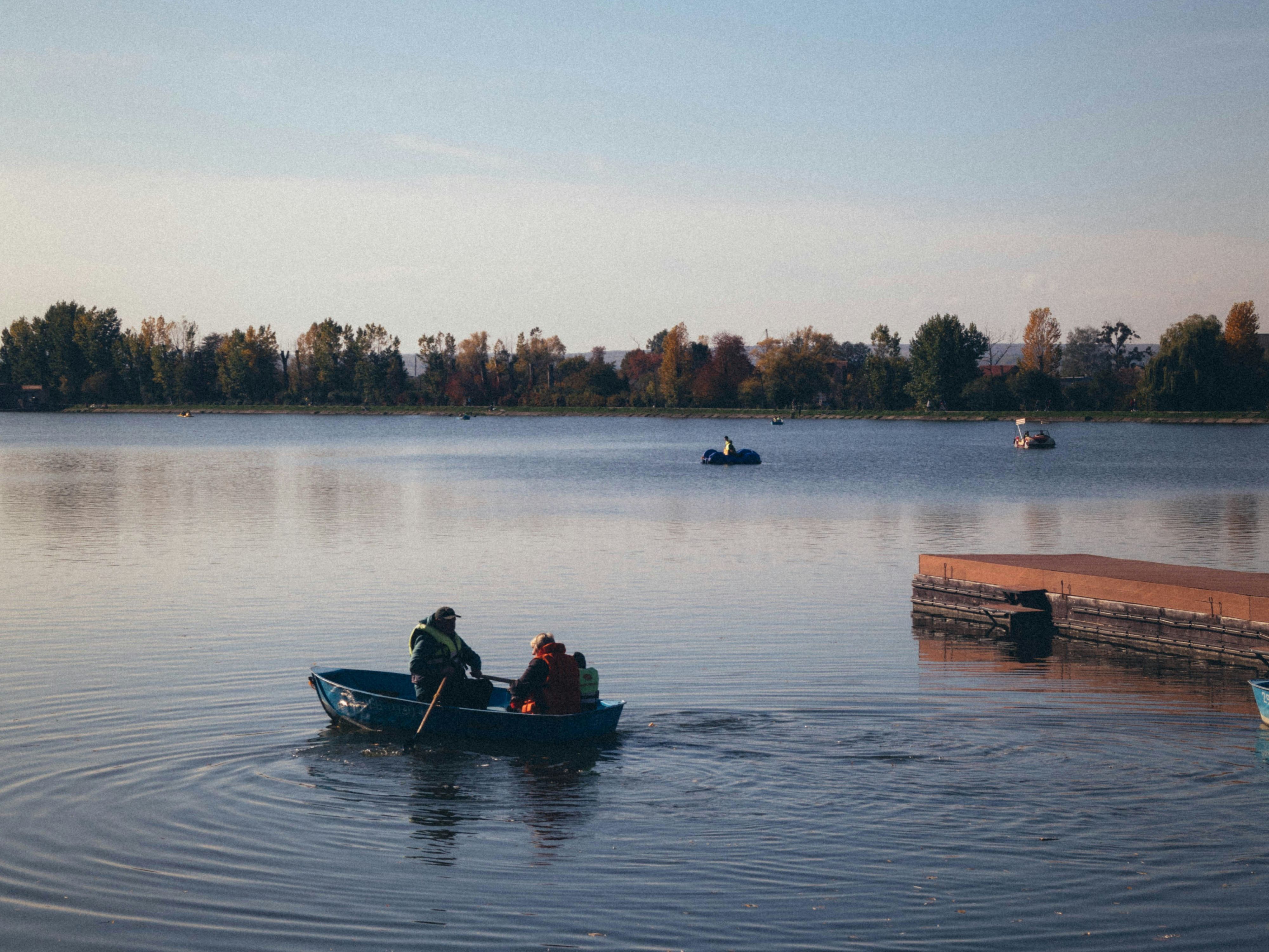 Two people rowing a small boat on a calm lake near a floating dock