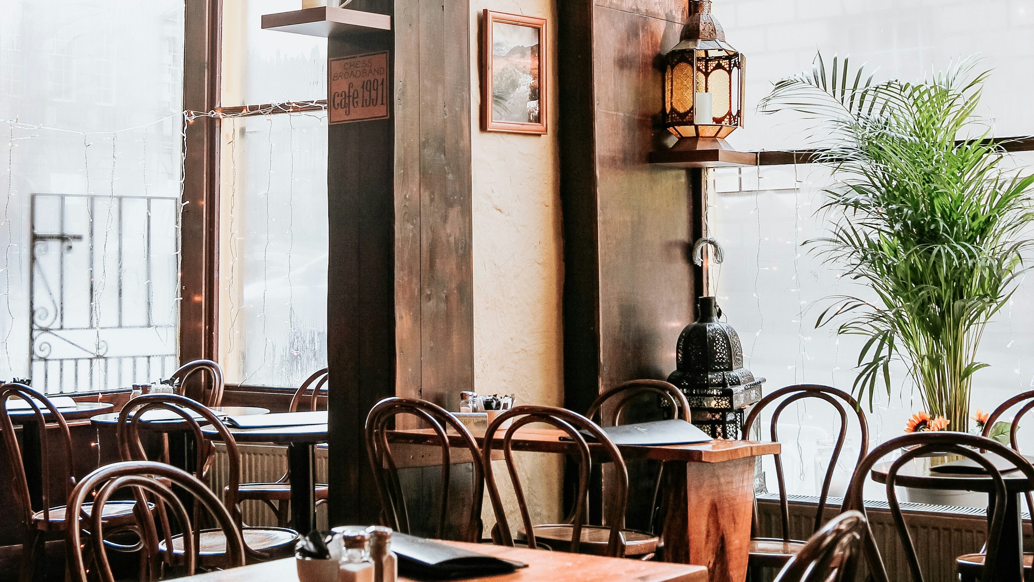 Cosy café interior with wooden tables, bentwood chairs and hanging pendant lights by large windows
