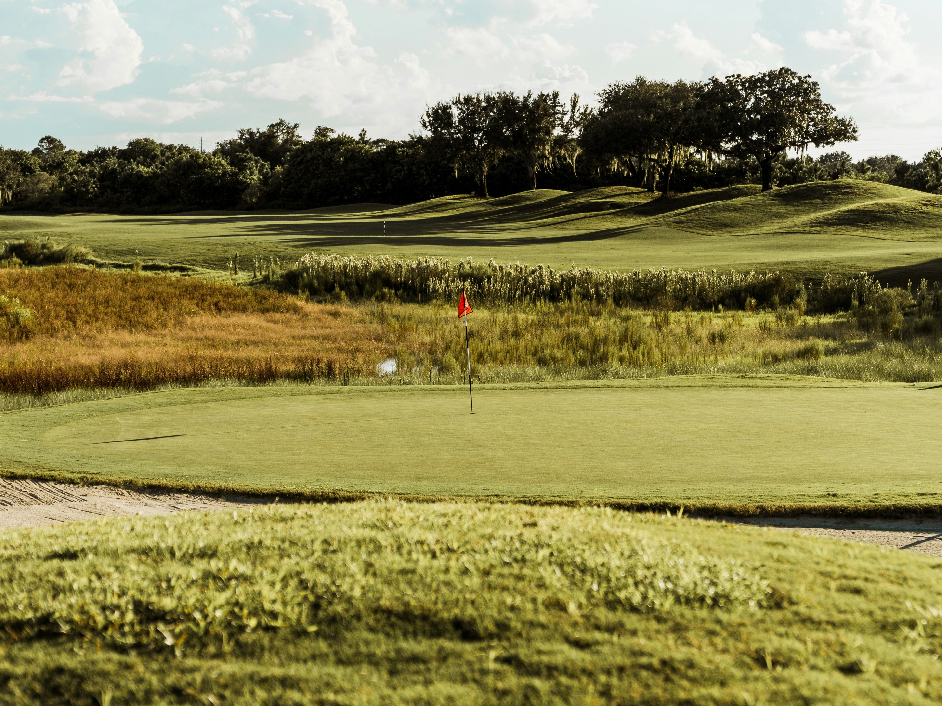Golf course green with a red flag and rolling fairways under a blue sky