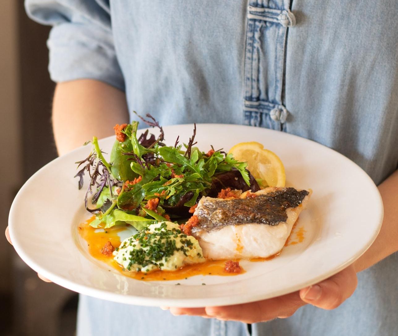 Person holding a plate with grilled fish, salad, and mashed potatoes