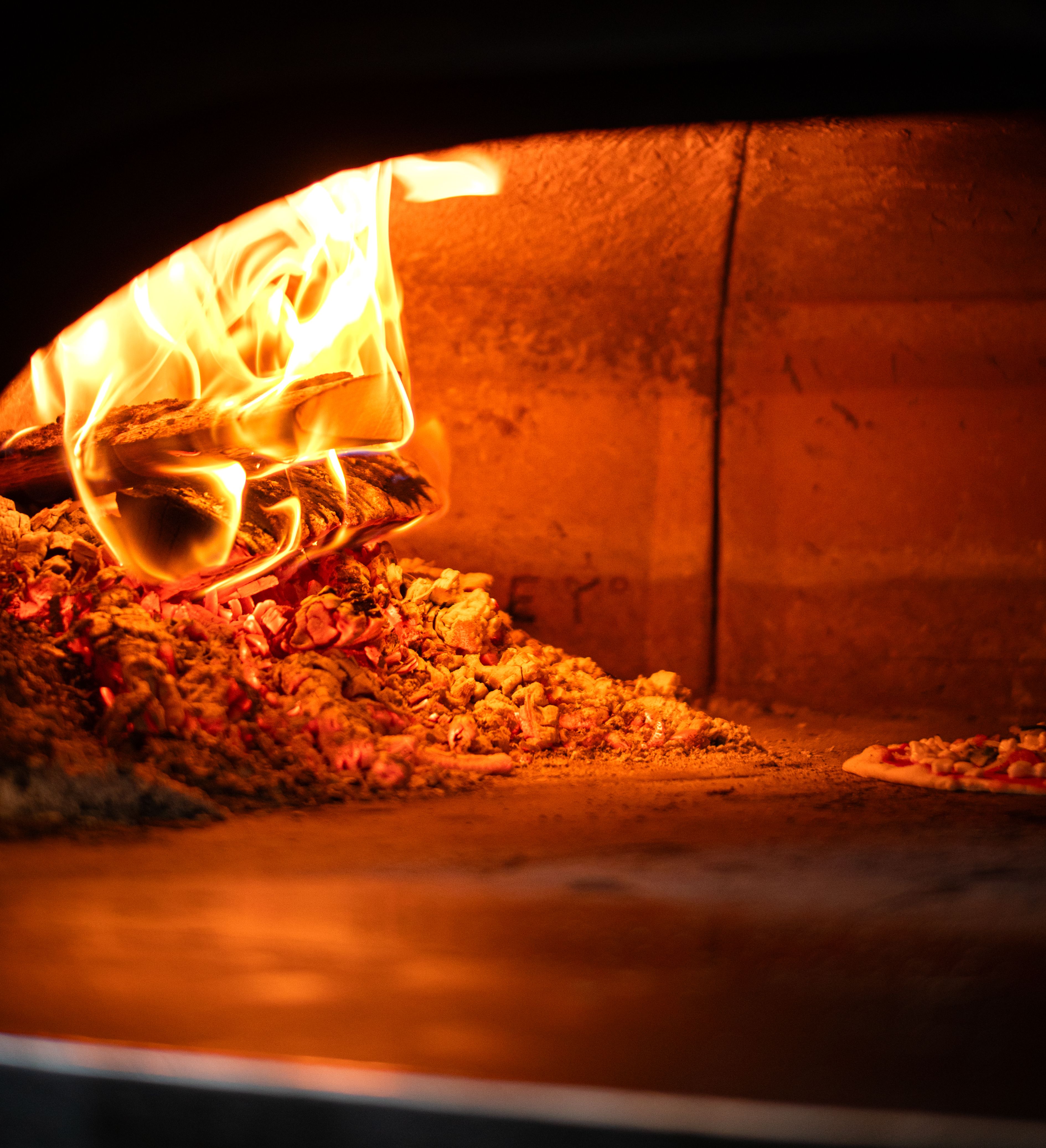 Wood-fired pizza oven with flames and glowing embers inside
