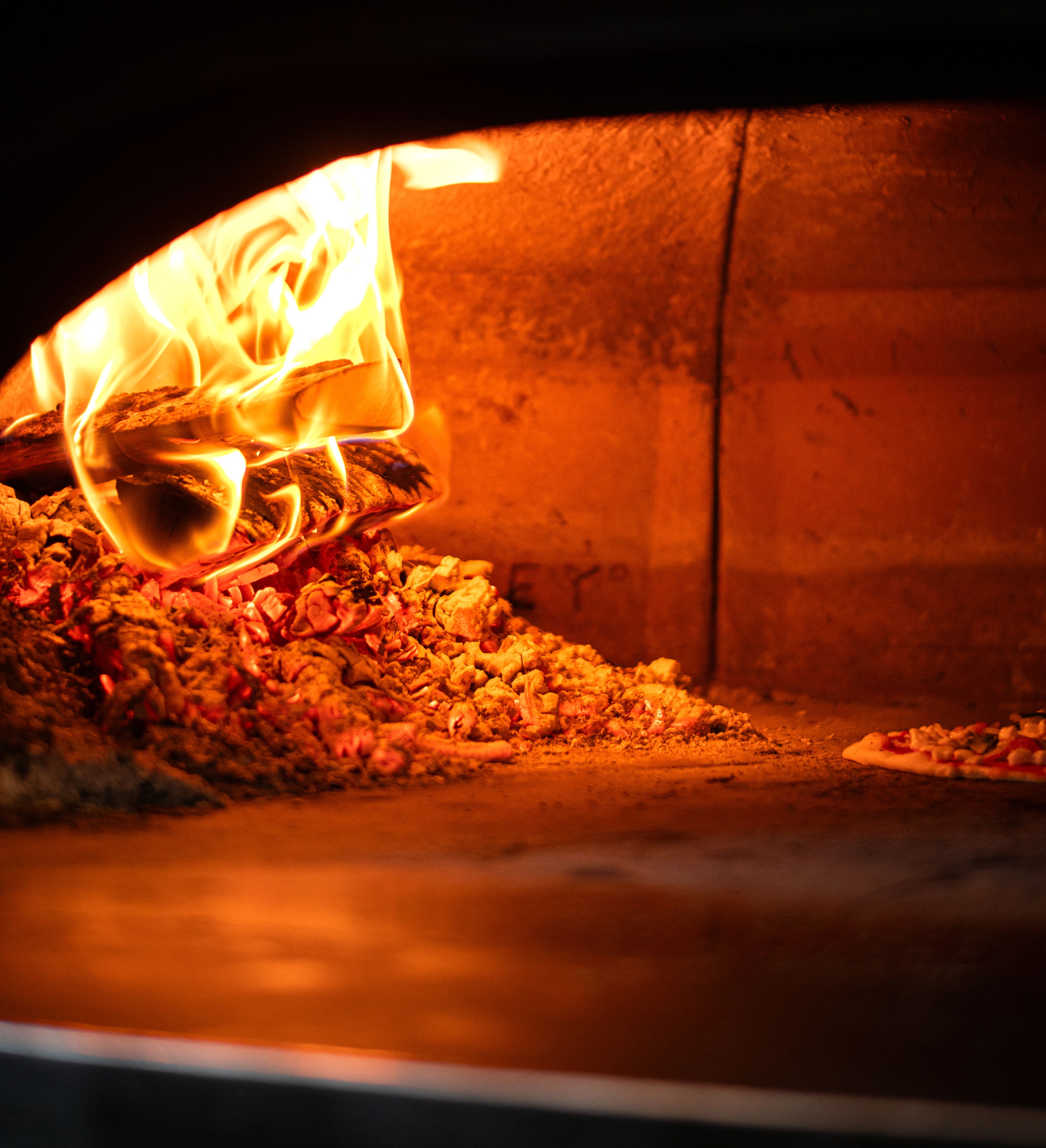 Wood-fired pizza oven with flames and glowing embers heating the stone floor