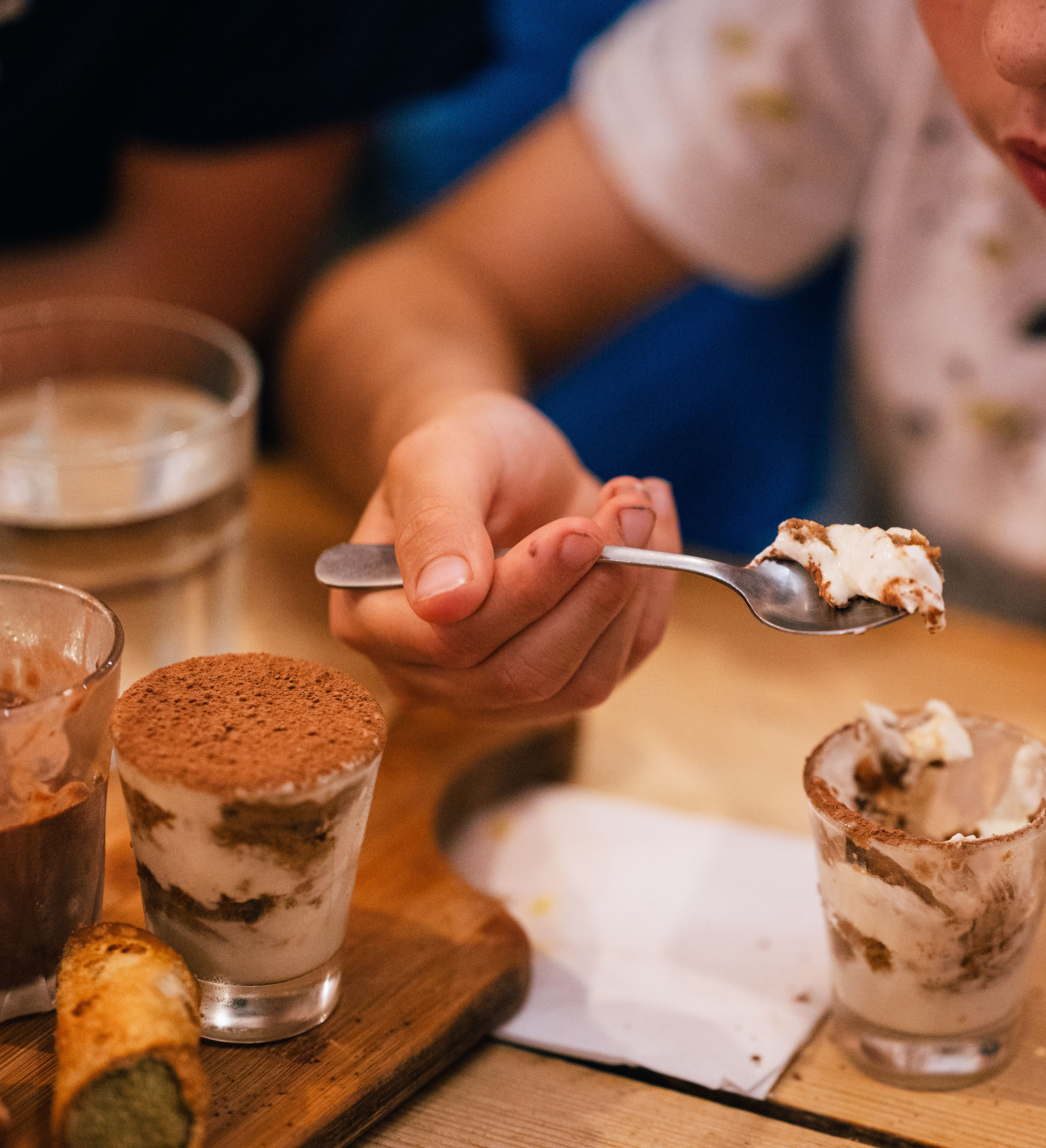 Child eating a spoonful of tiramisu dessert at a restaurant table