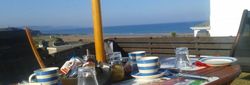 Outdoor breakfast table set with blue and white striped dishes, overlooking a beach and ocean view.