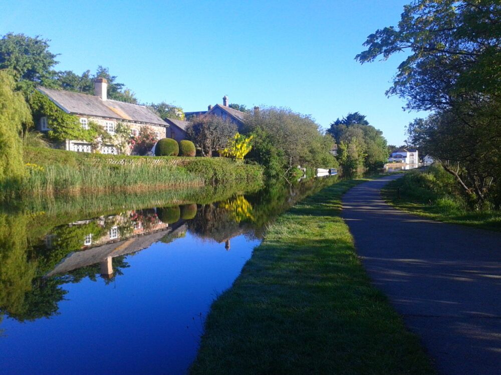 Country cottages beside a calm canal with a walking path and trees.