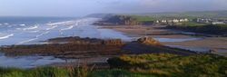 Coastal landscape with waves, rocky shore, sandy beach, and distant seaside village under a blue sky
