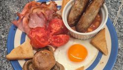Traditional English breakfast with bacon, sausages, baked beans, grilled tomato, mushrooms, egg, and toast.