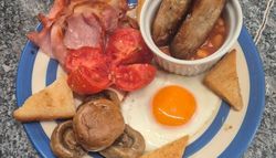 Traditional English breakfast with bacon, sausages, baked beans, grilled tomato, mushrooms, egg, and toast.