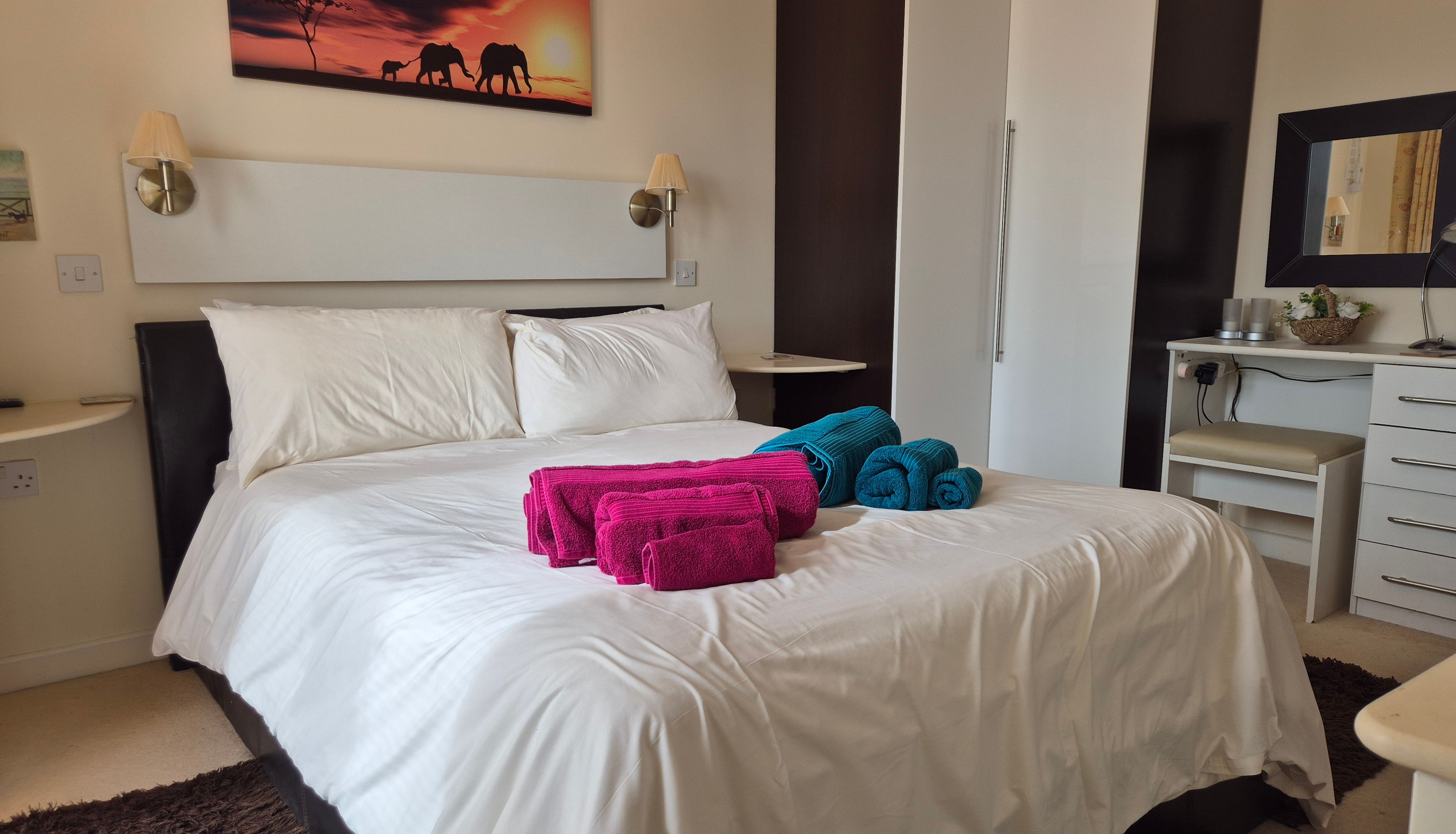 Modern bedroom with white bedding, colorful towels on the bed, and elephant wall art.