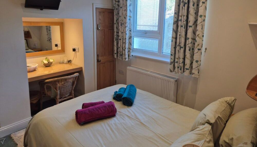 Cozy bedroom with window, curtains, bed, and a small workspace with mirror.
