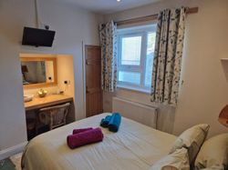 Cozy bedroom with window, curtains, bed, and a small workspace with mirror.