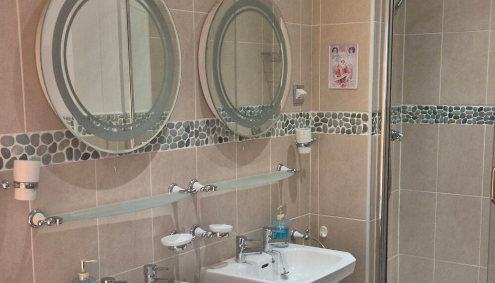 Modern bathroom with double sinks, two round mirrors, and a shower enclosure.