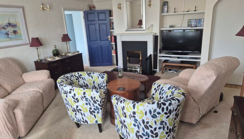 Cozy living room with two patterned chairs, two beige armchairs, a television, and a fireplace.