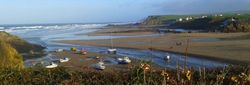 Boats resting on sand at low tide on a wide, scenic beach with waves and cliffs in the distance.