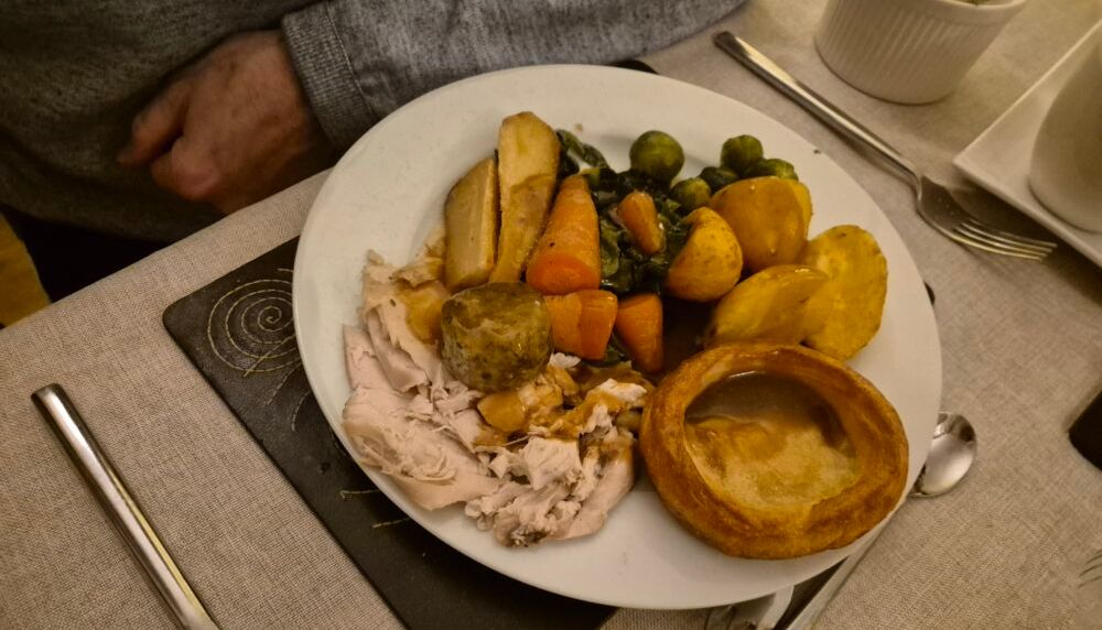 A plate of traditional roast dinner with turkey, potatoes, vegetables, stuffing, and Yorkshire pudding.