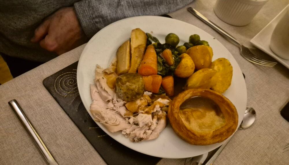 A plate of traditional roast dinner with turkey, potatoes, vegetables, stuffing, and Yorkshire pudding.