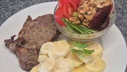 Plate with steak, creamy sliced potatoes, and a side salad with tomatoes, cucumber, beets, walnuts, and onions