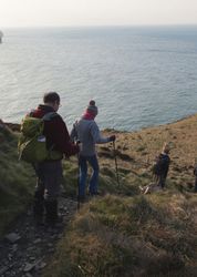 Group of hikers descending a grassy coastal cliff with the sea in the background
