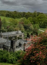 Historic stone manor house surrounded by lush green gardens and trees under a cloudy sky