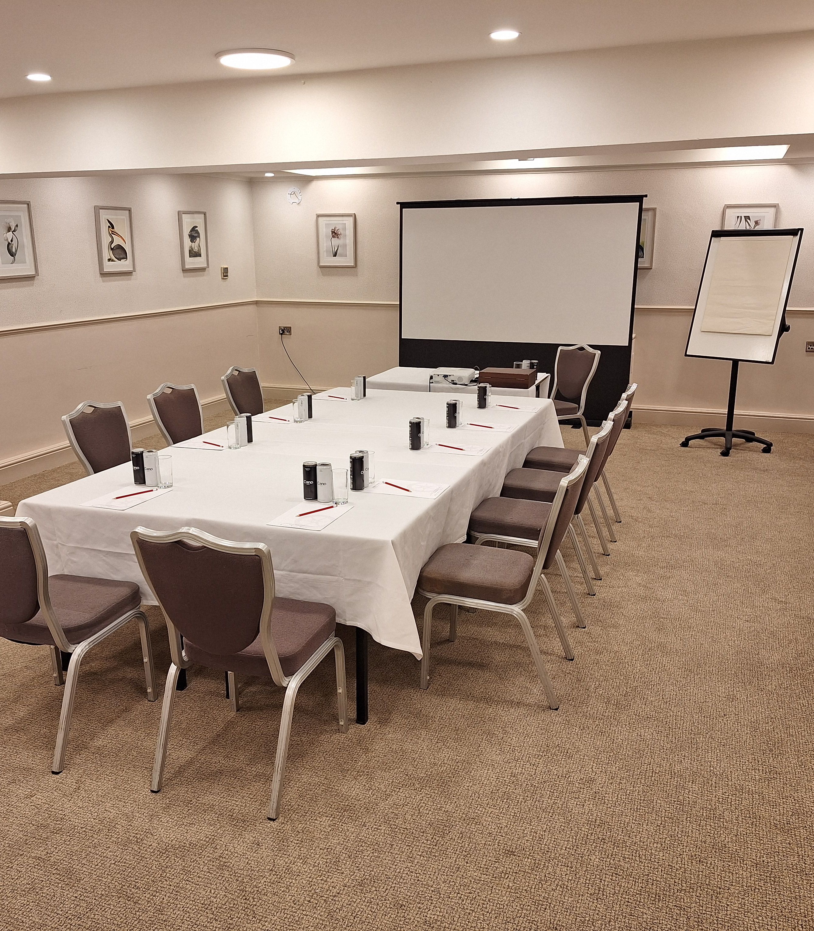 Conference room with a rectangular table, chairs, projector screen, and flip chart.
