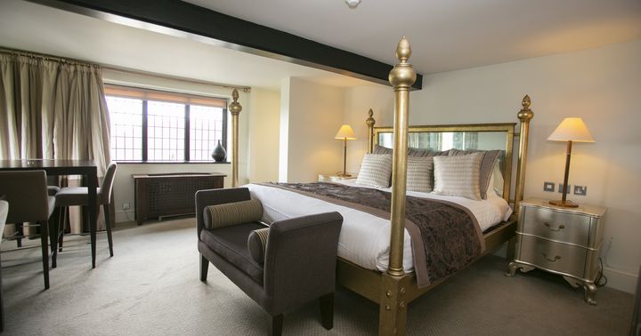 Elegant hotel room with a four-poster bed, upholstered bench, and bedside lamps