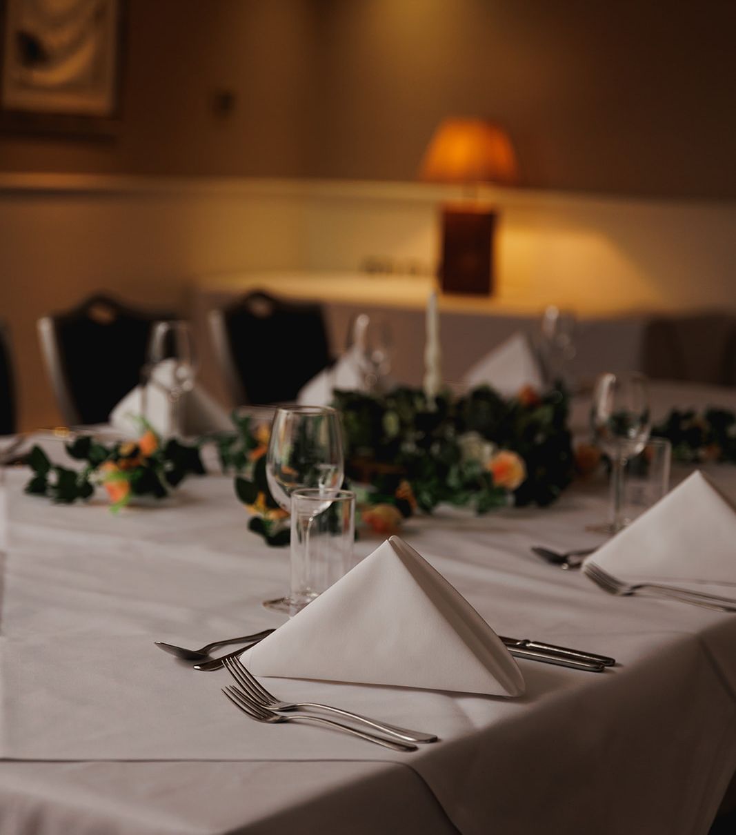 Elegant table setting with white napkins, glassware, and floral centerpiece in a dimly lit room.