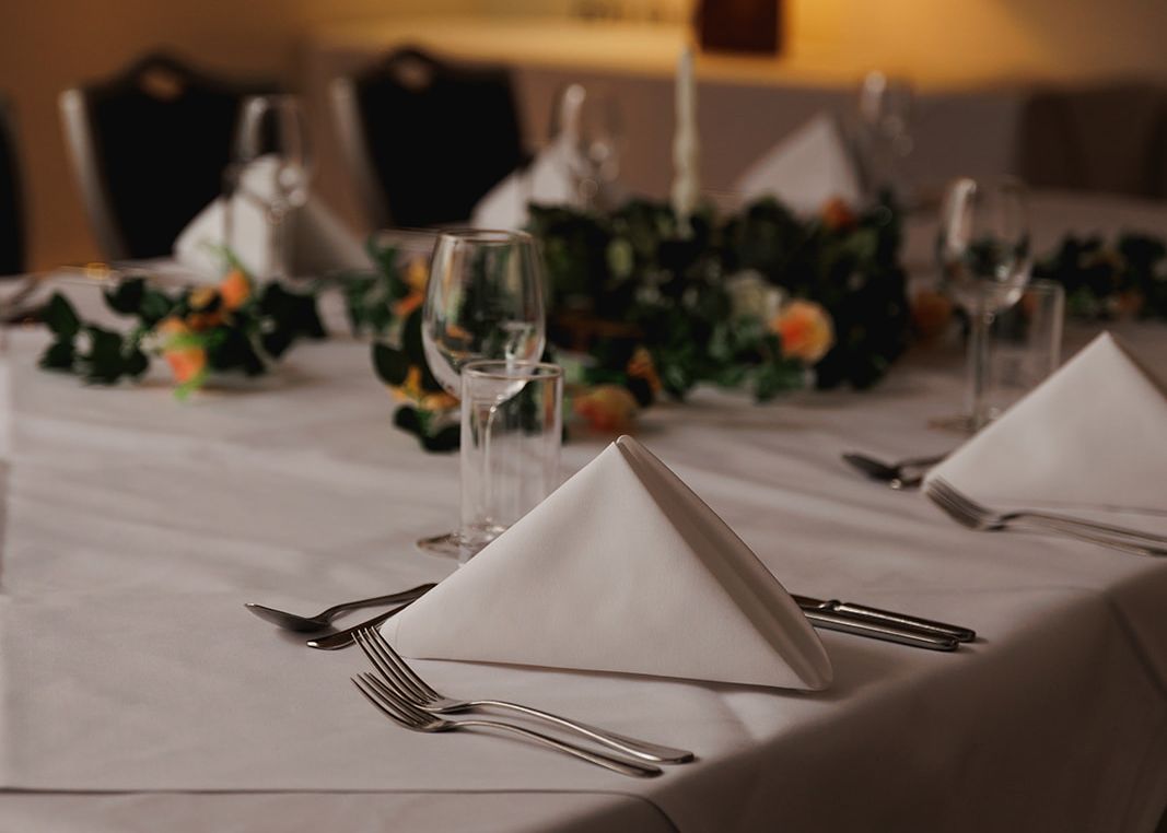 Elegant table setting with white napkins, glassware, and floral centerpiece in a dimly lit room.
