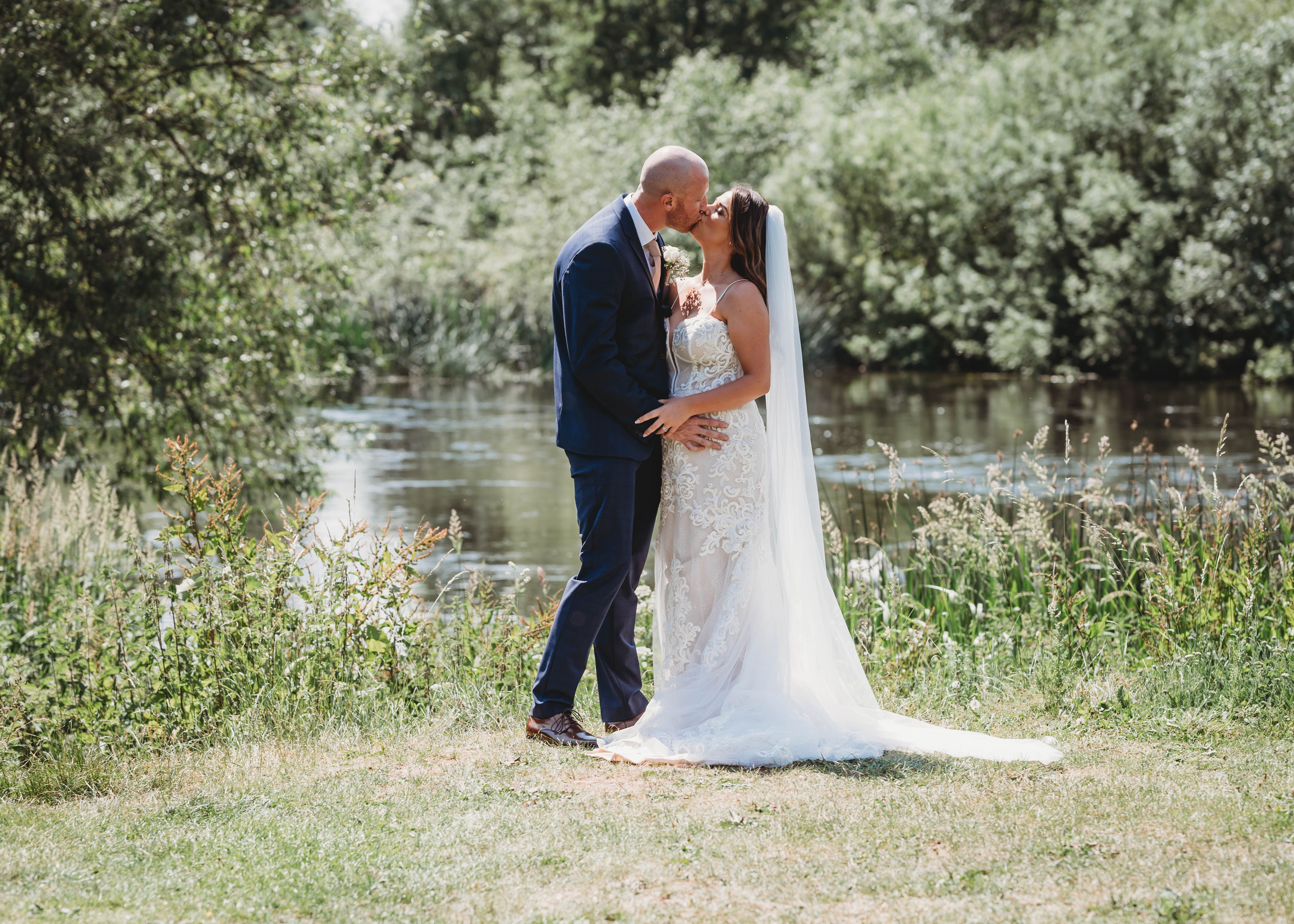 Bride and groom kissing outdoors near a pond