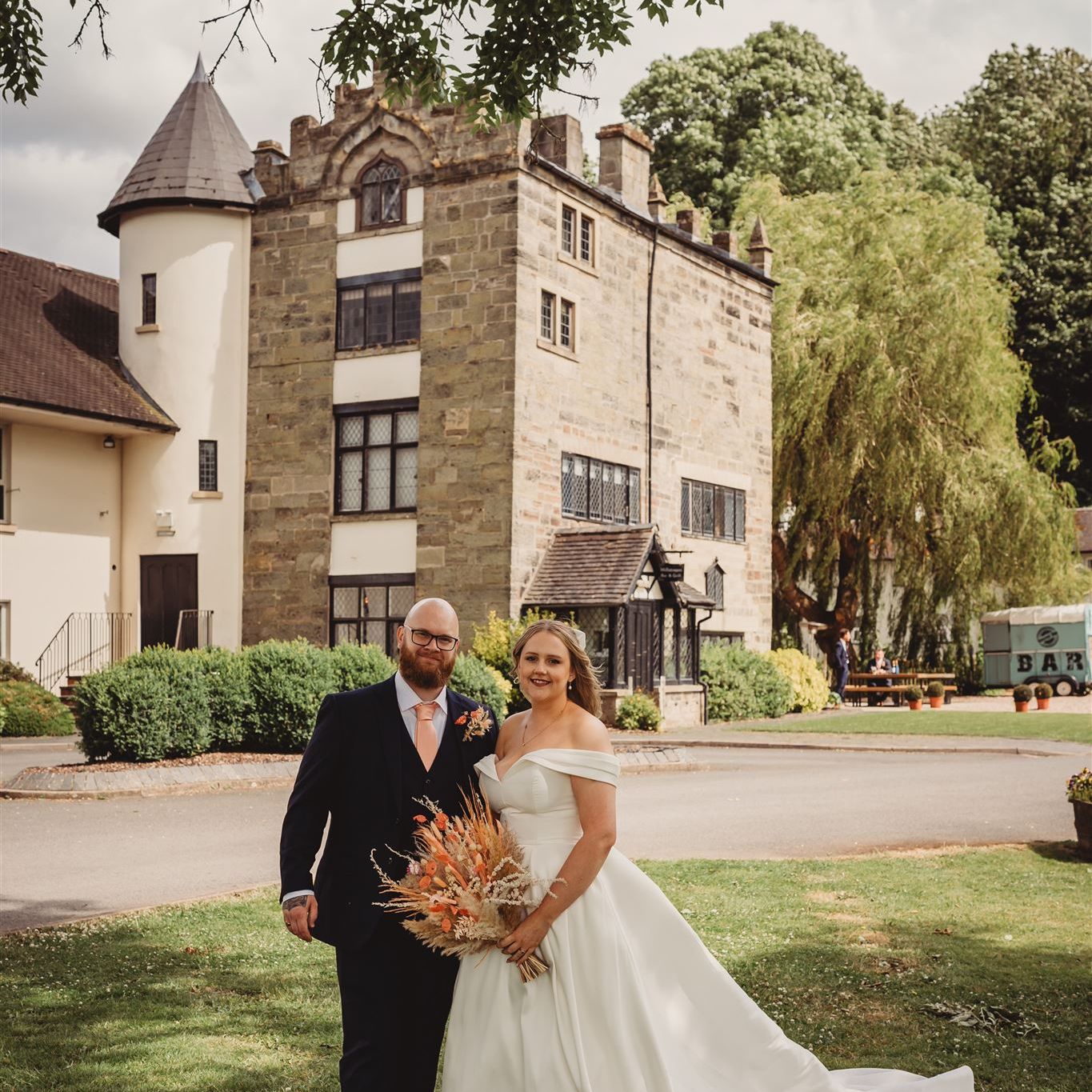 Bride and groom posing outside in front of a historic stone building on their wedding day.