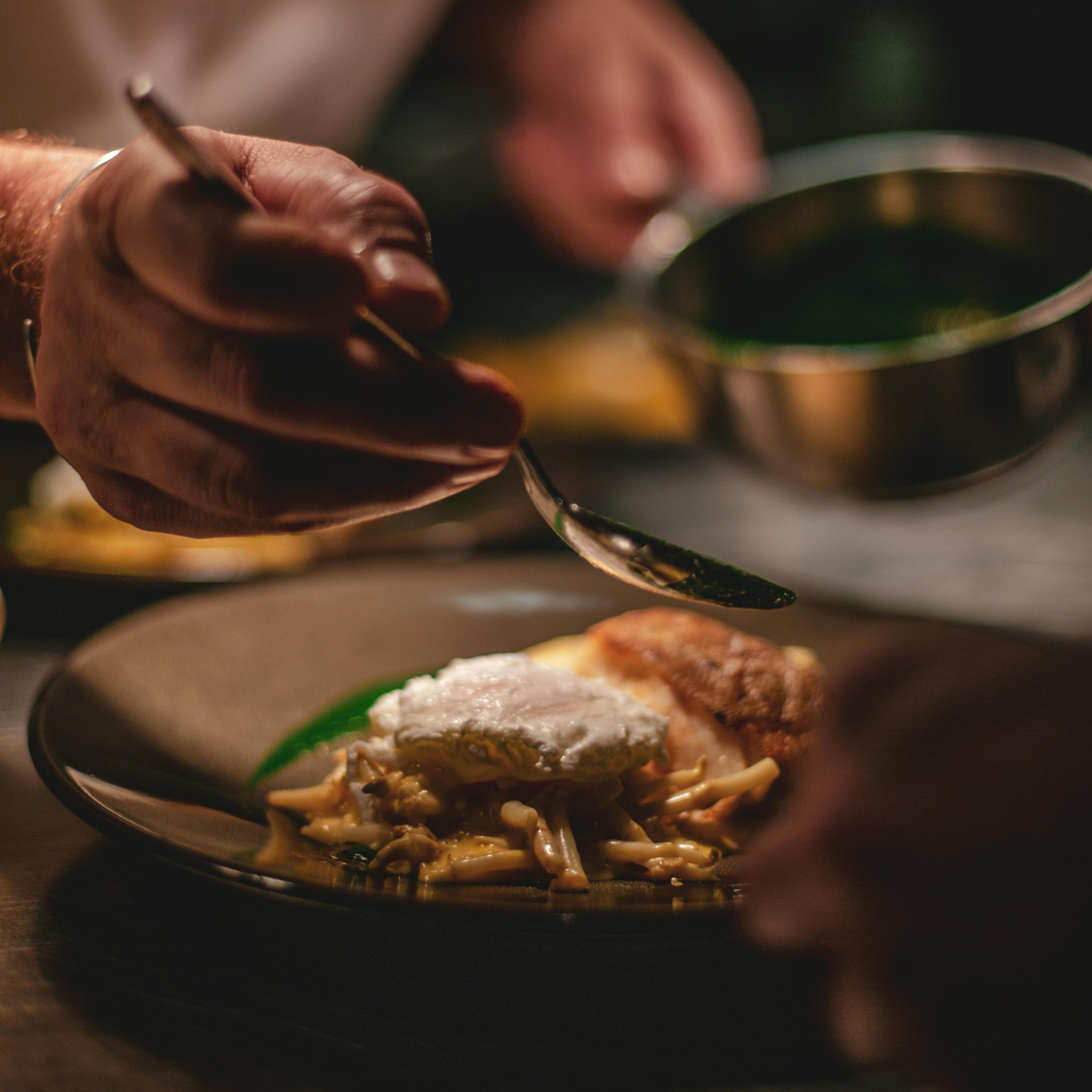 Close-up of a chef plating a gourmet dish with delicate sauce and a poached egg.
