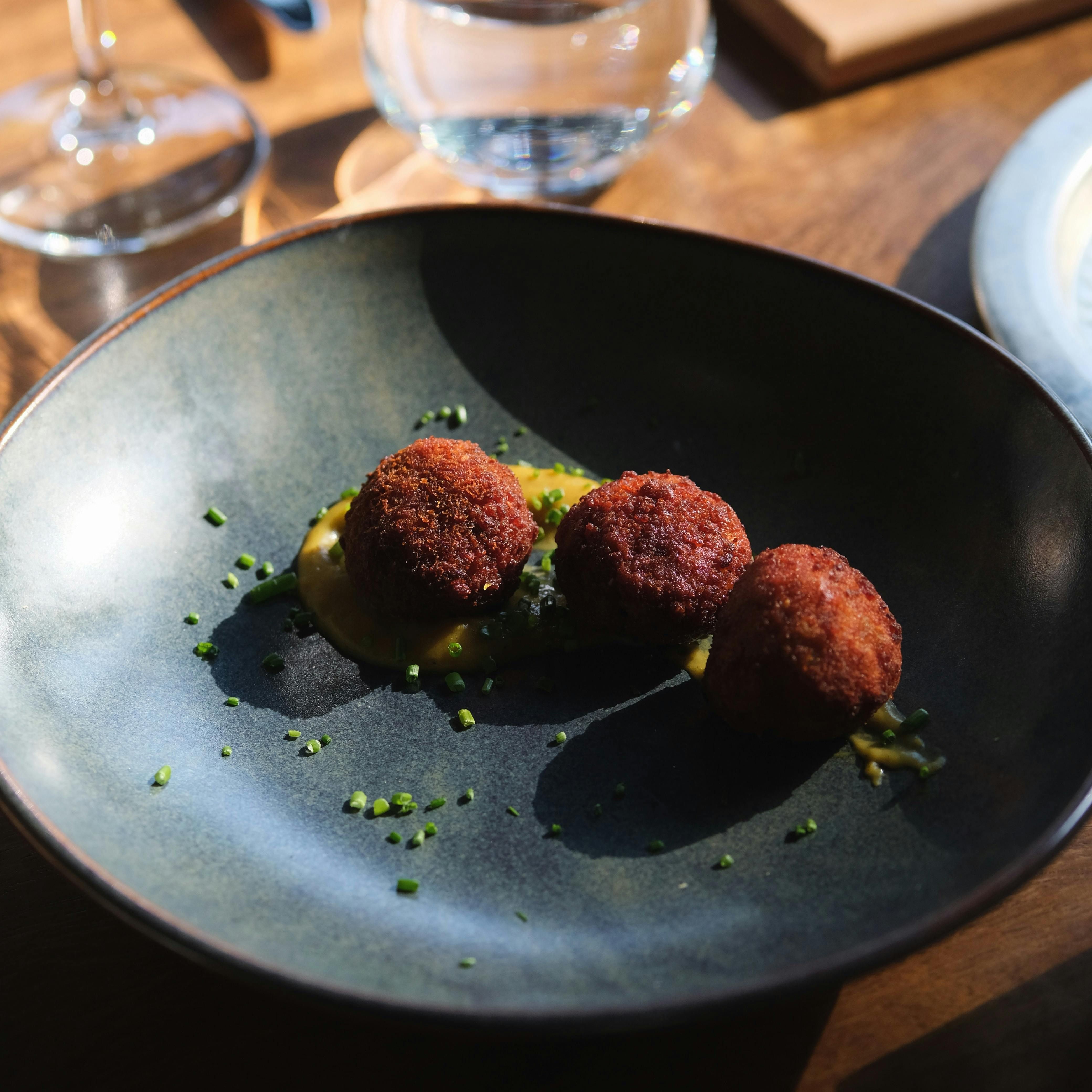 Three breaded and fried balls served on a blue plate with yellow sauce and green garnish.