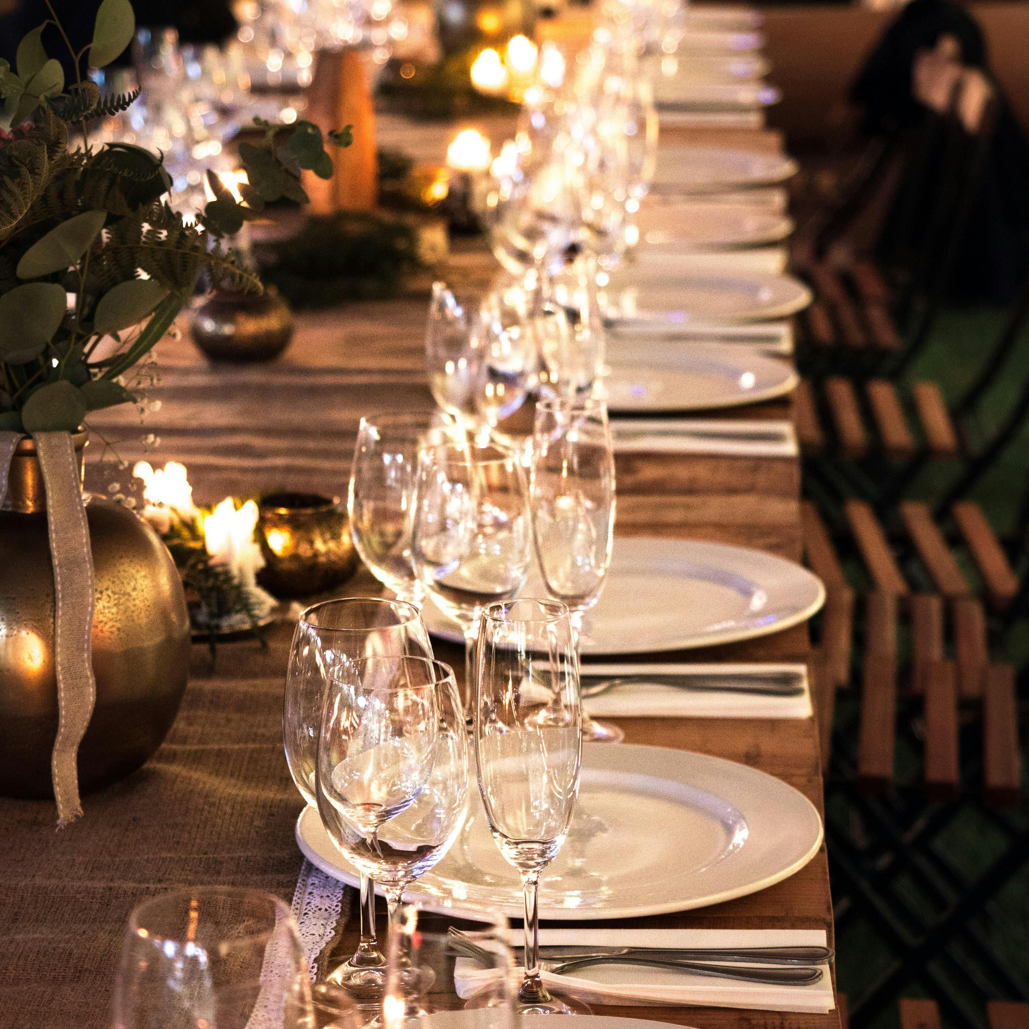 Elegant dinner table set with white plates, wine glasses, napkins, cutlery, candles, and floral centerpieces