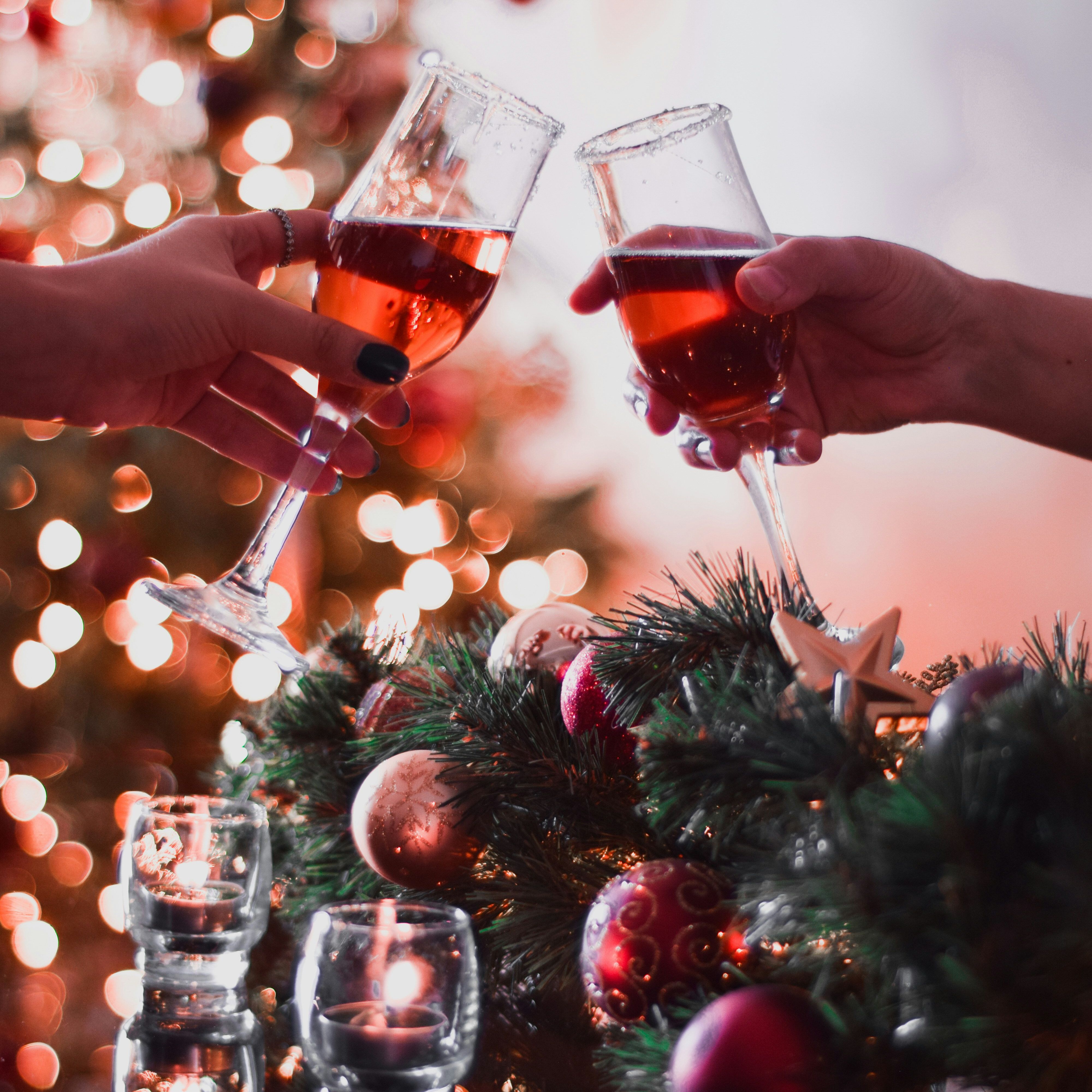 Two people clinking glasses of red champagne in front of a decorated Christmas tree