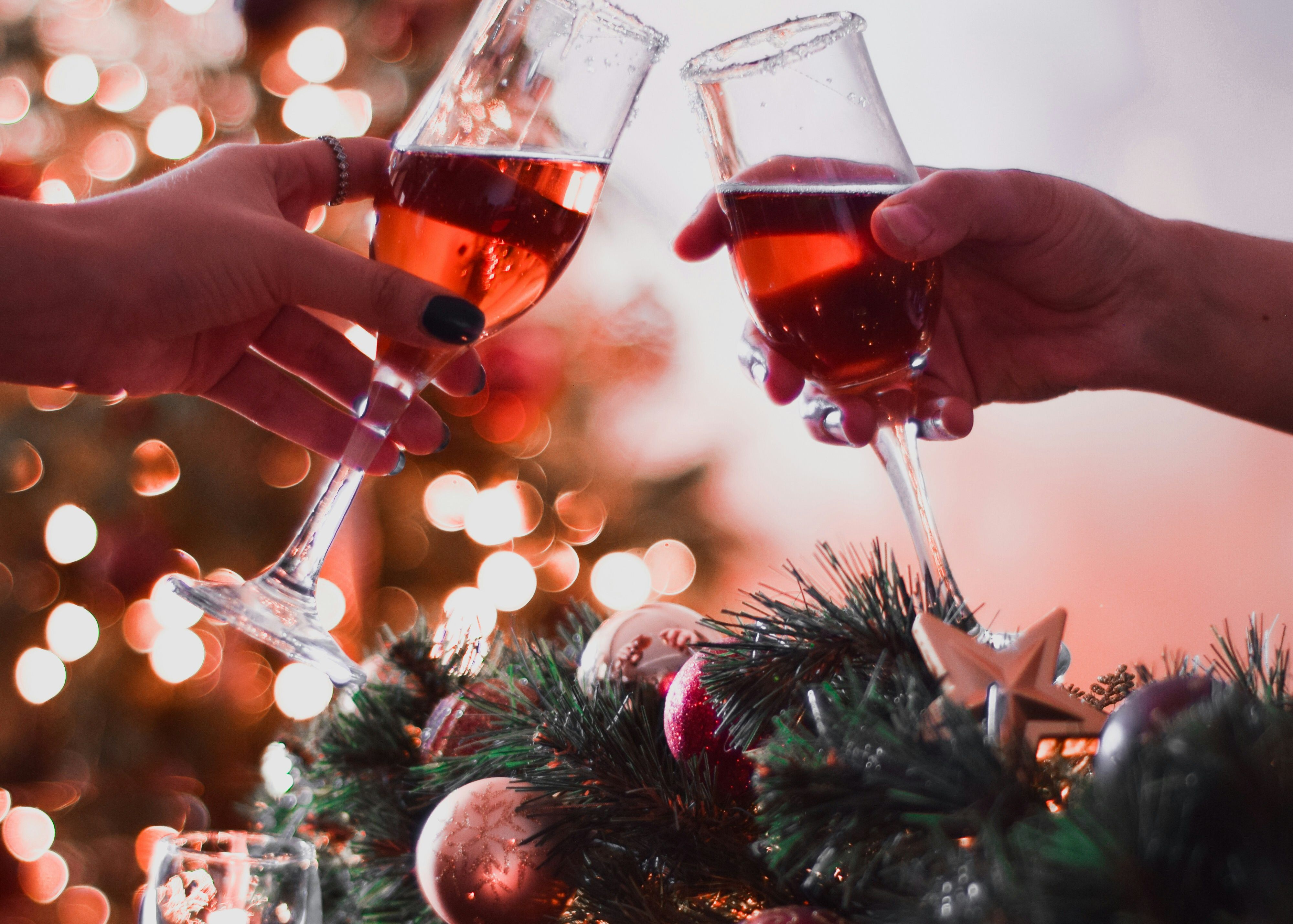 Two people clinking glasses of red champagne in front of a decorated Christmas tree