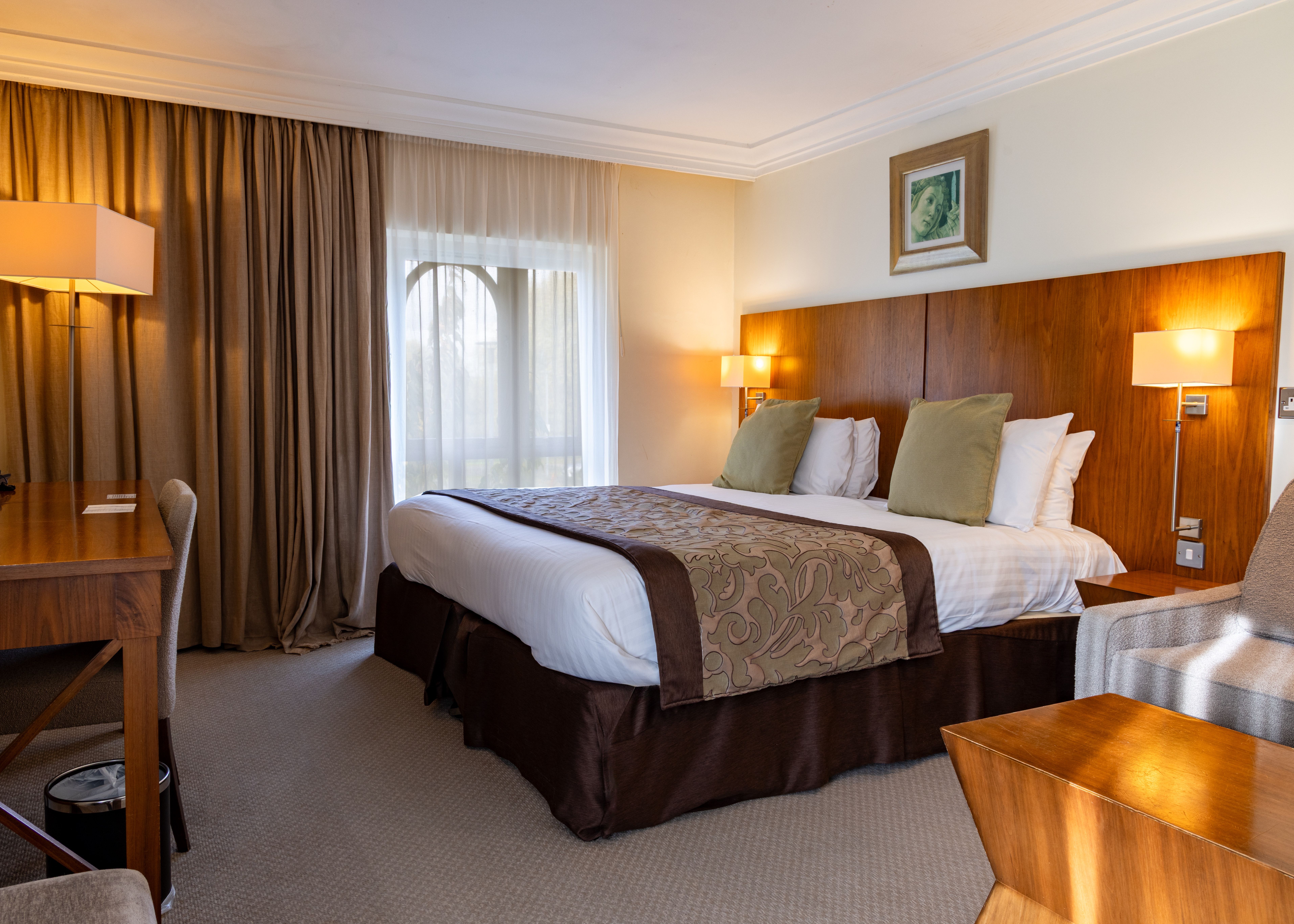 Deluxe hotel room with a large bed, wooden furniture, desk, and cozy lighting