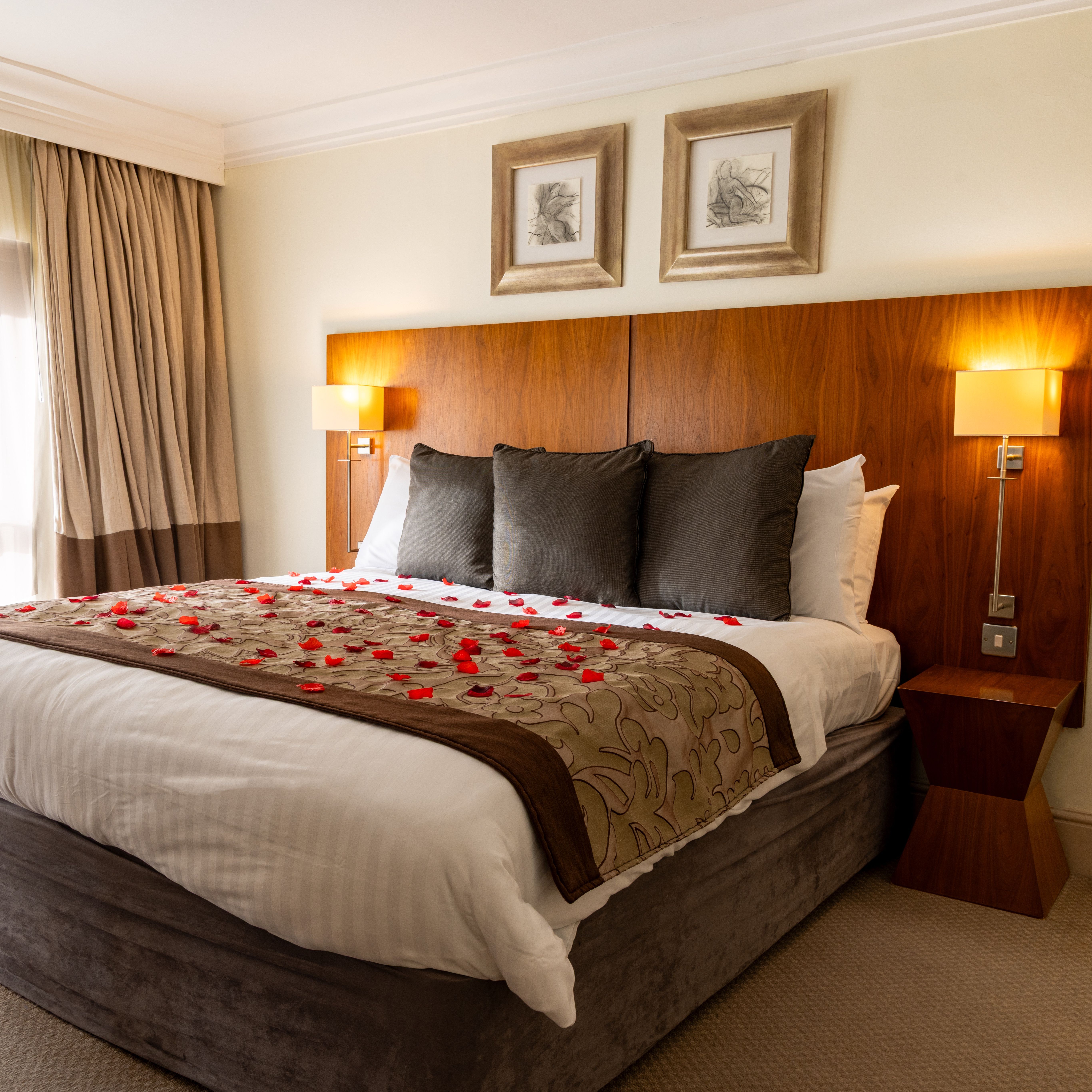 Hotel suite with a decorated bed, rose petals, plush pillows, and modern wooden headboard