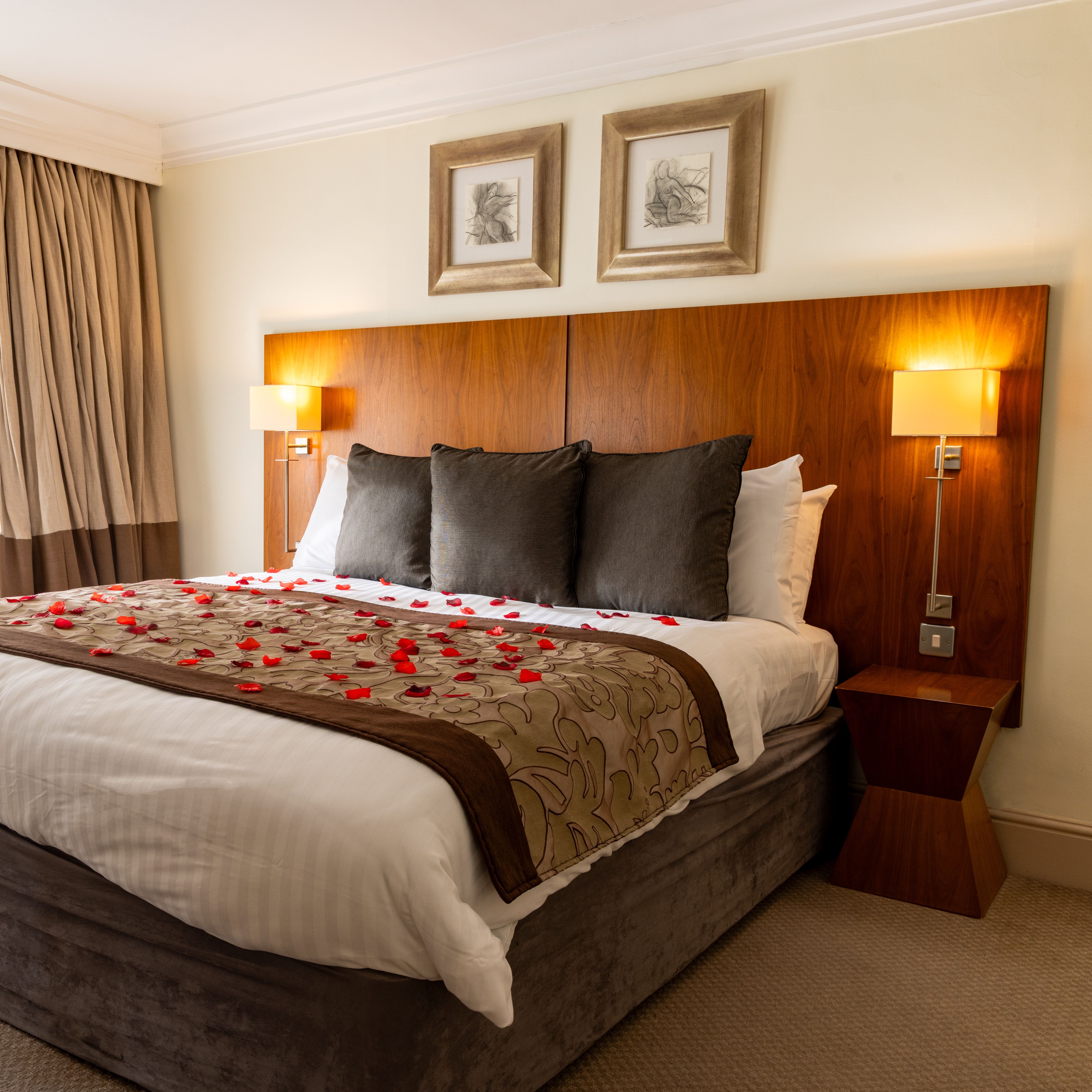 Hotel suite with a decorated bed, rose petals, plush pillows, and modern wooden headboard
