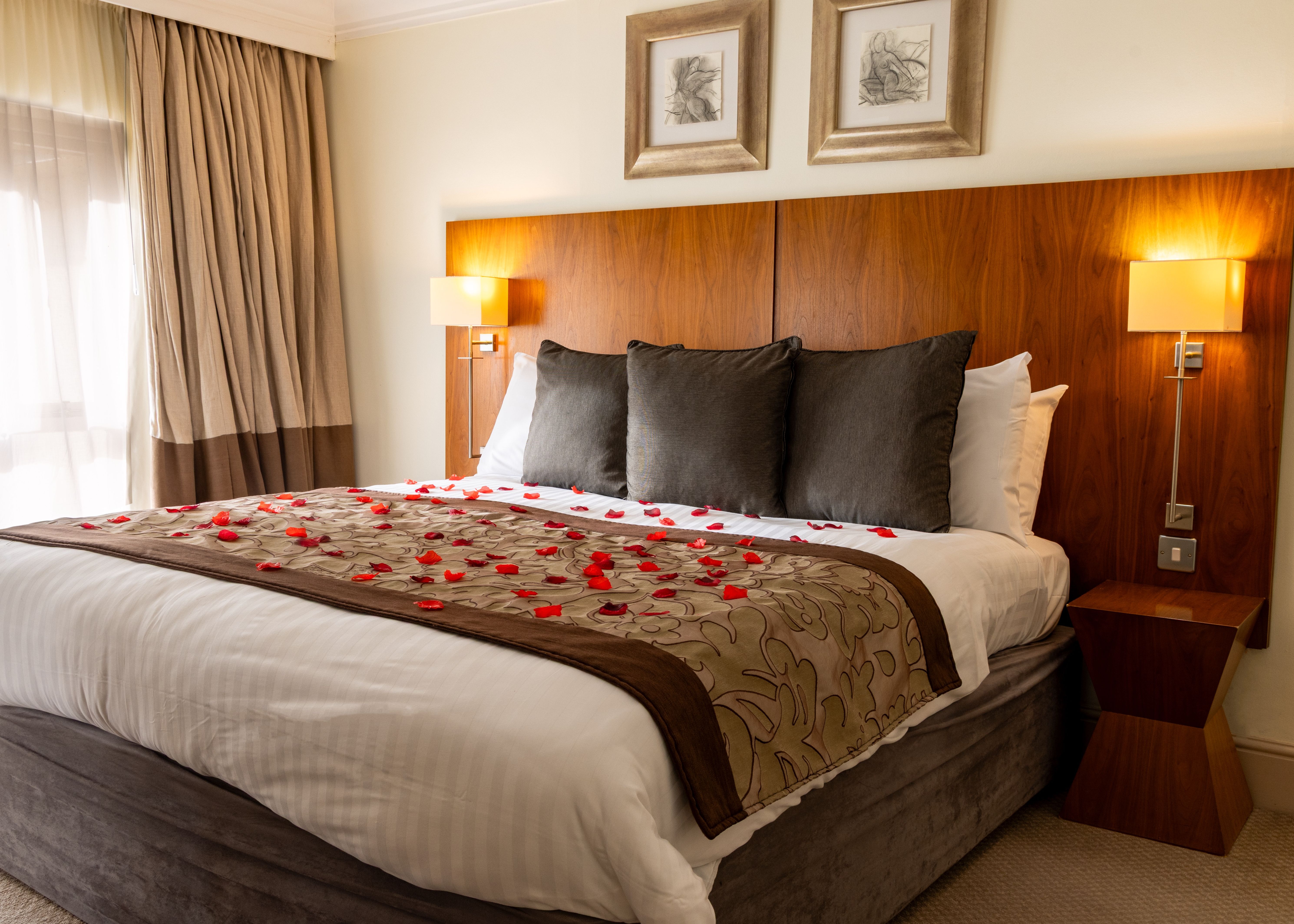 Hotel suite with a decorated bed, rose petals, plush pillows, and modern wooden headboard
